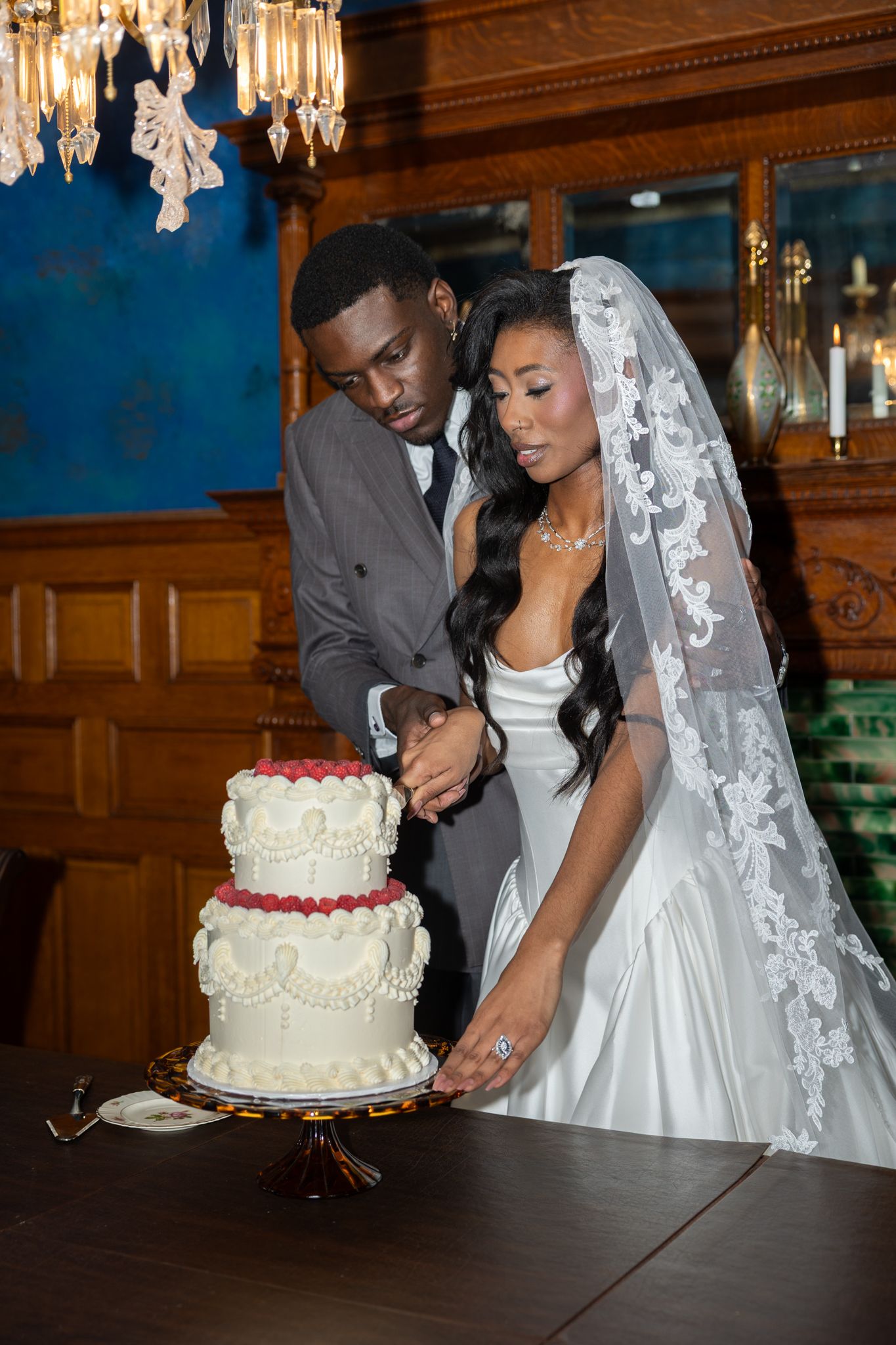 Newlywed couple cutting a white tiered wedding cake with red berries in an elegant wood-paneled reception venue in Buffalo New York