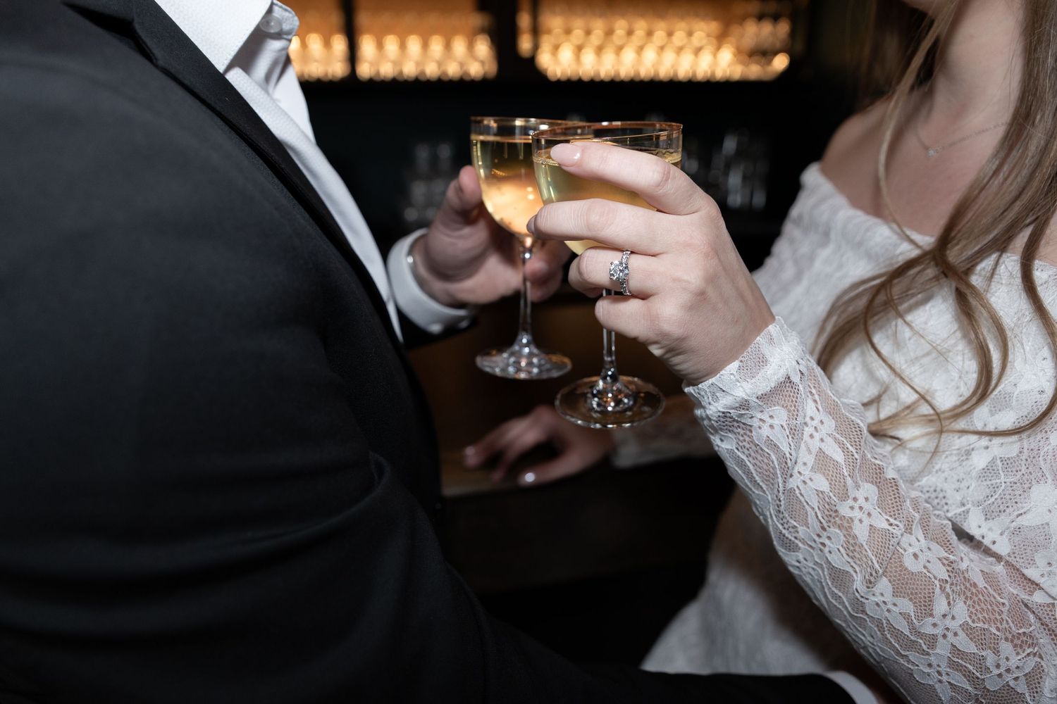 Bride and groom clinking champagne glasses in elegant wedding attire, celebrating their reception with sparkling wine.