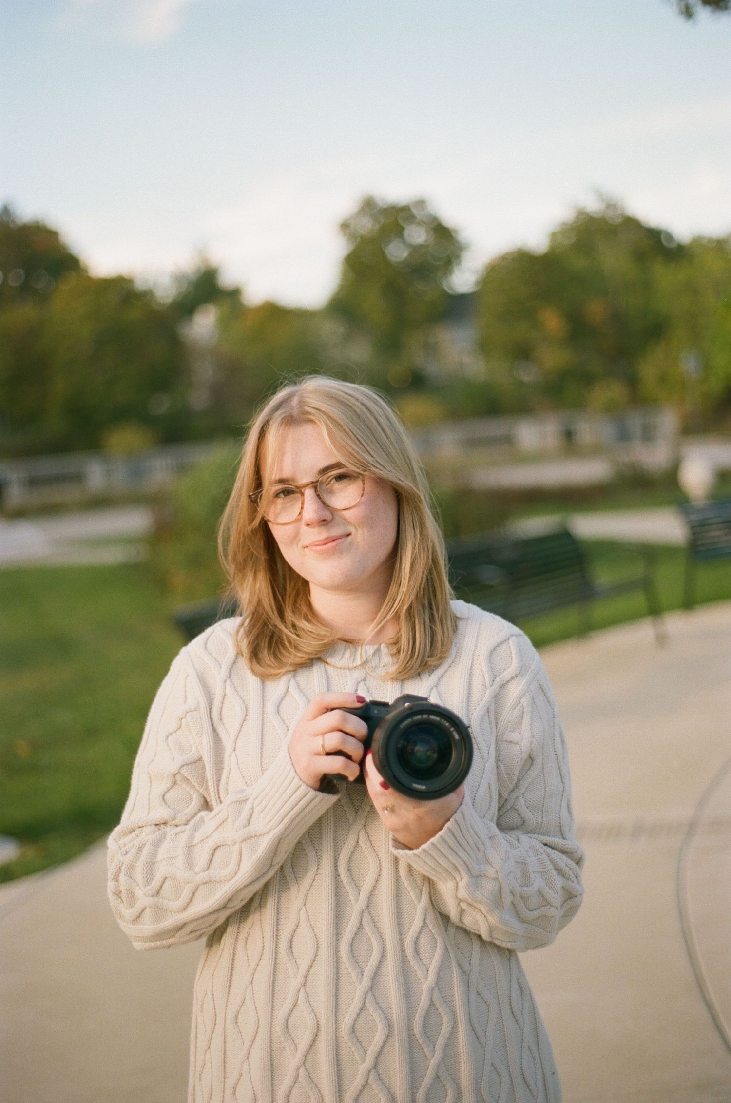 Photographer in cable knit sweater takes photos outdoors in warm light.