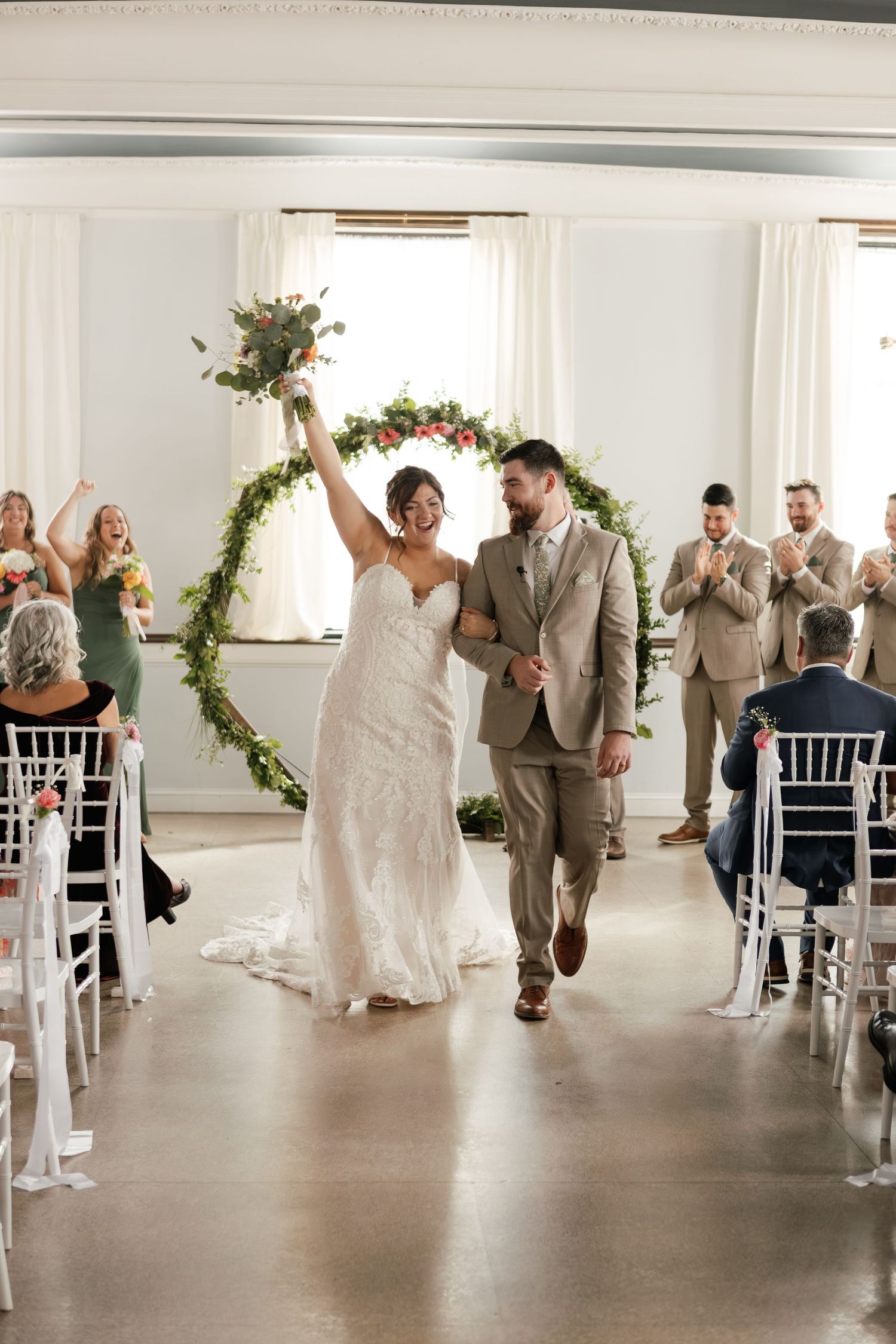 Couple and wedding party in khaki suits and white dresses dance during reception celebration.