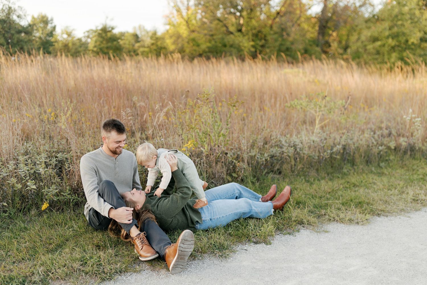 A couple relaxing together on a path beside a field of tall grass during sunset.