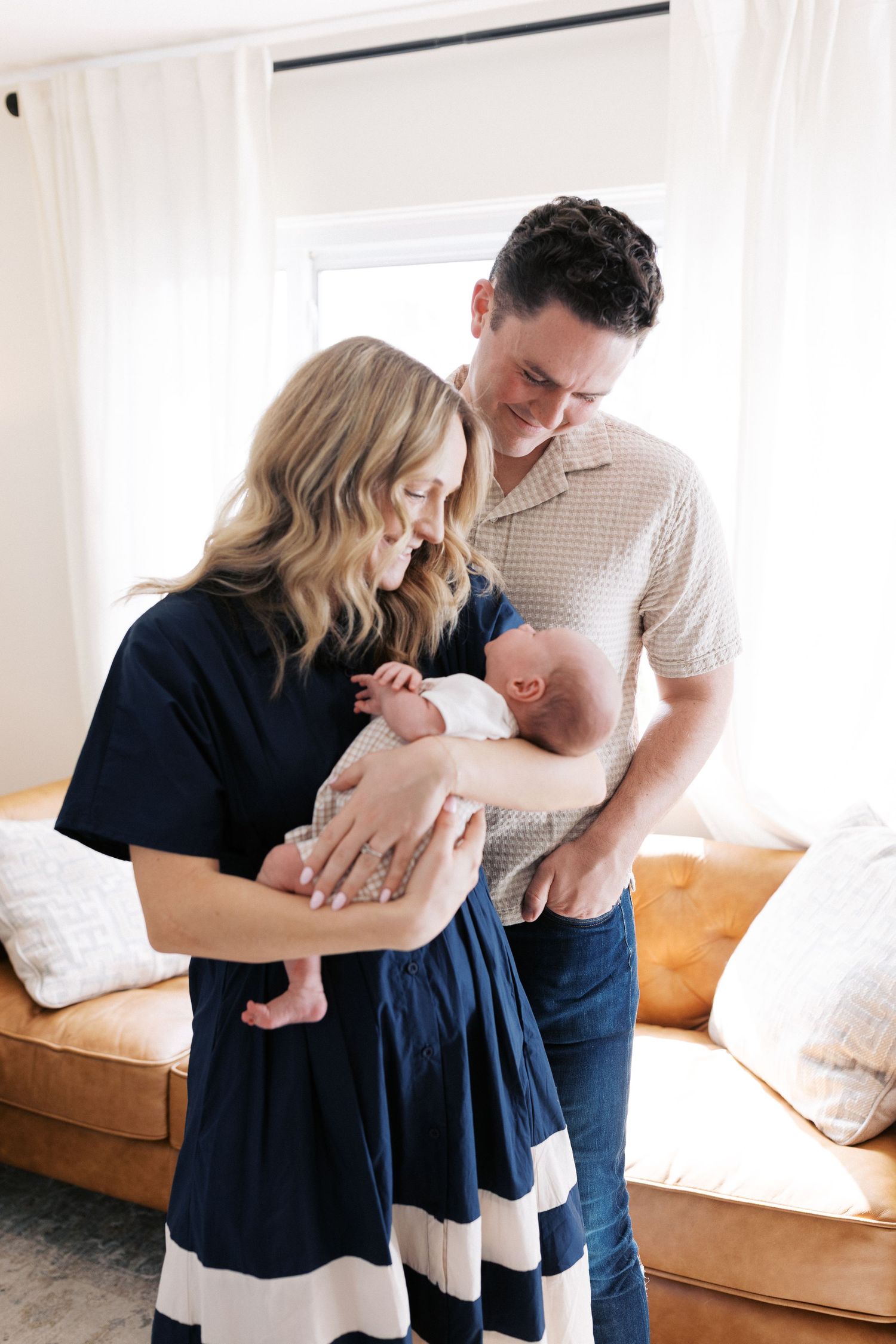 Parents sharing a tender moment with their newborn baby in a bright living room.