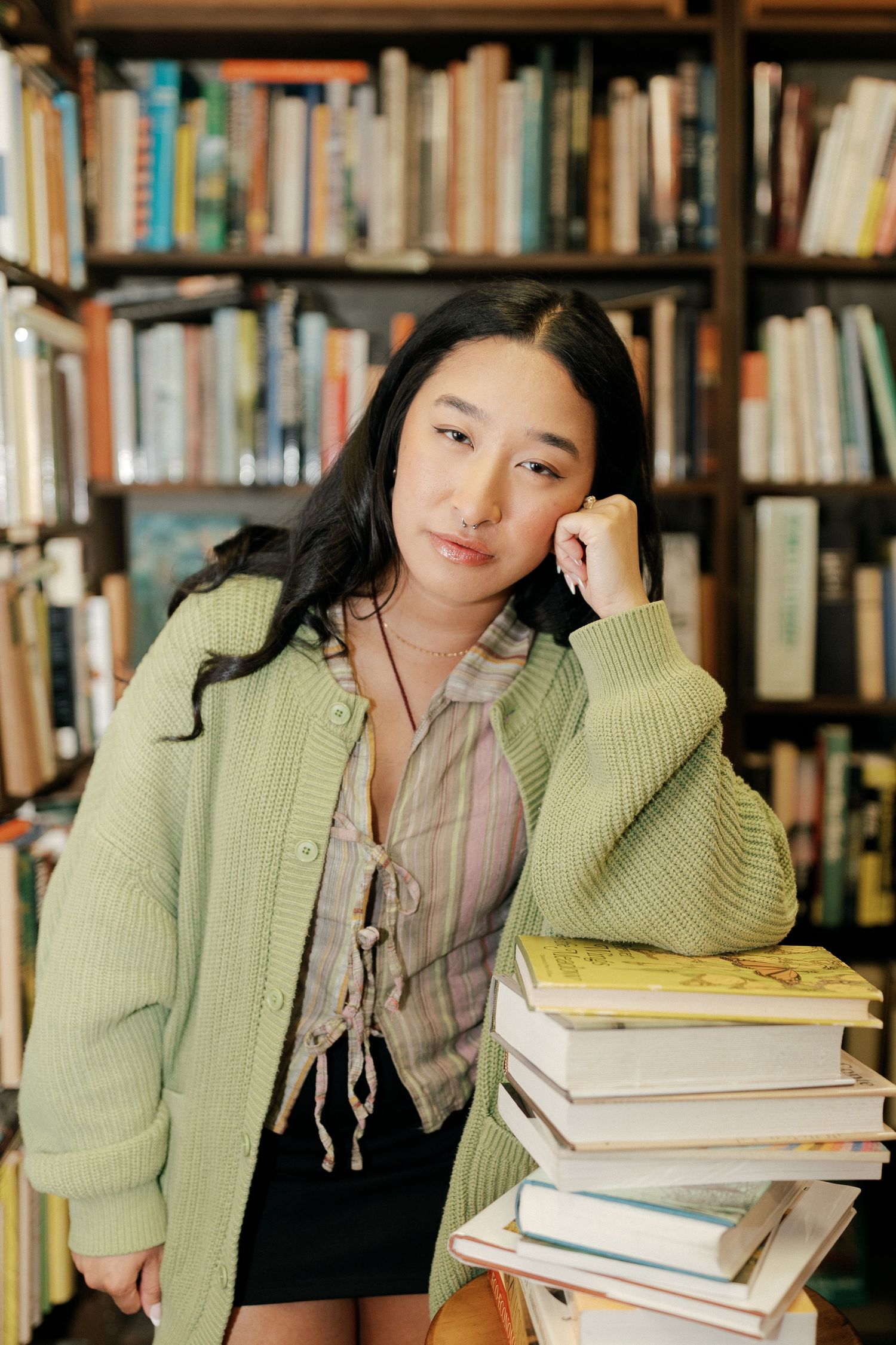Student in green sweater studying with stack of books in library.