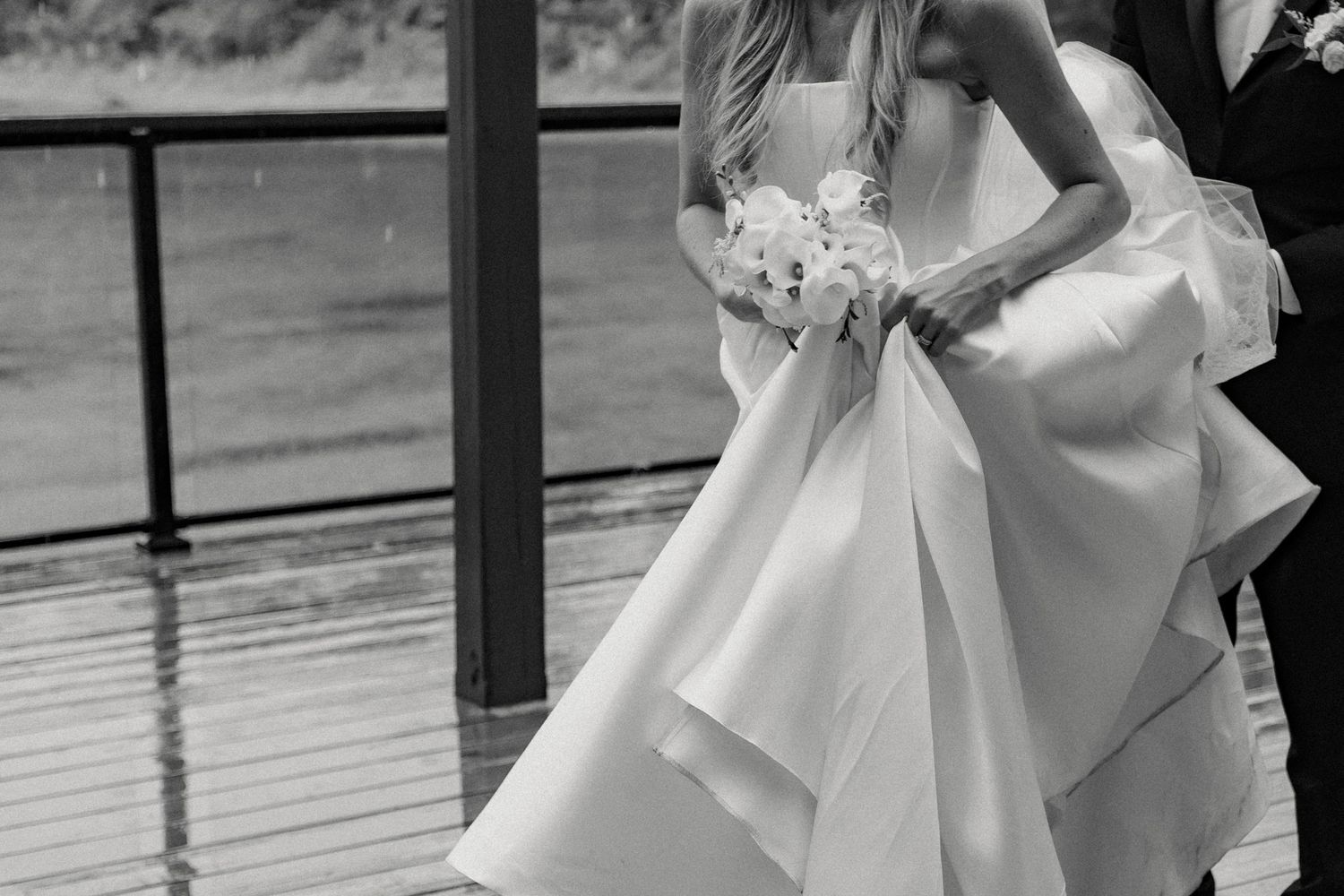 Close-up black and white photo of an elegant white wedding dress with flowing fabric details.