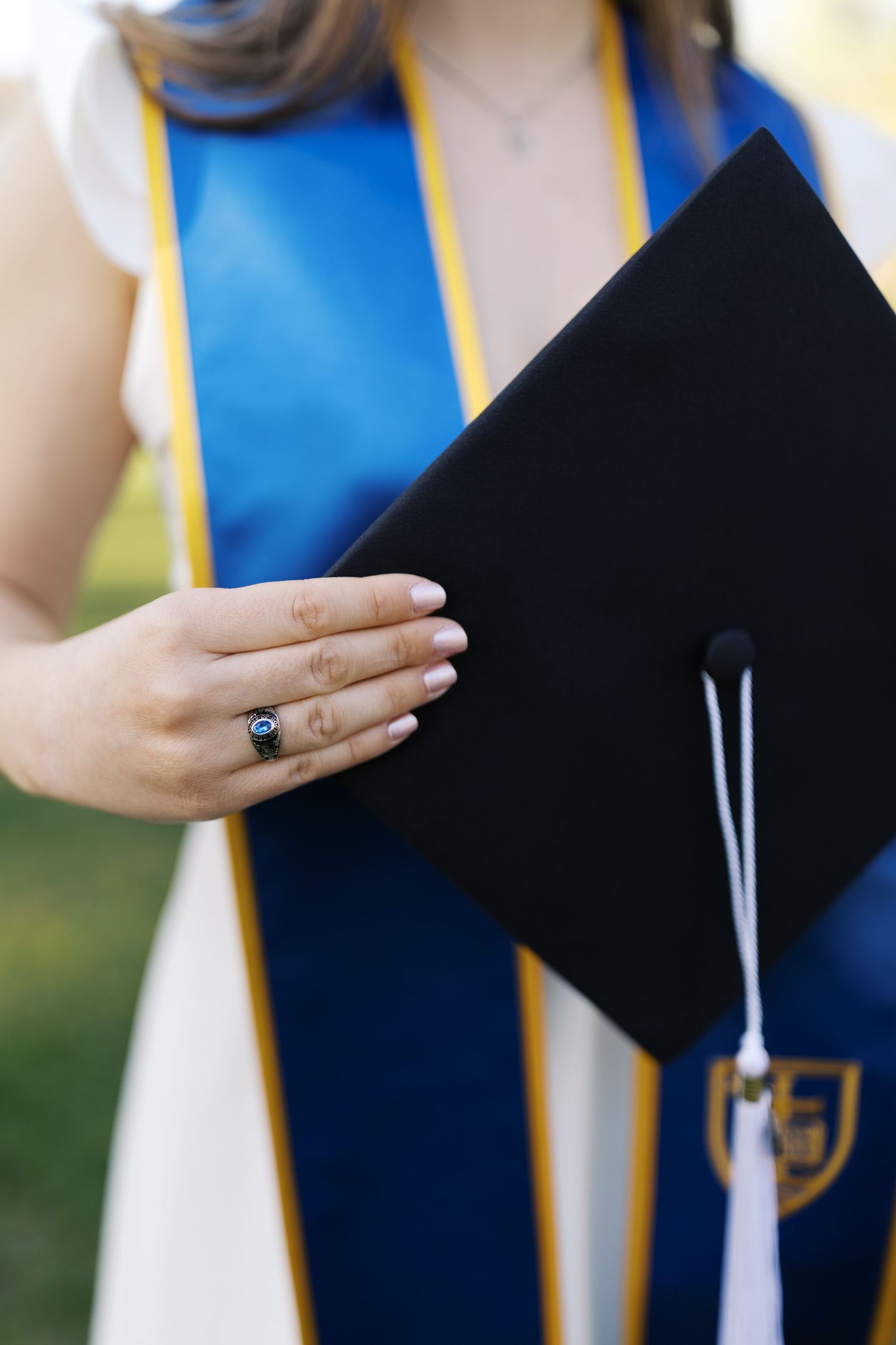 Close-up of graduation cap and gown with blue and gold stole.