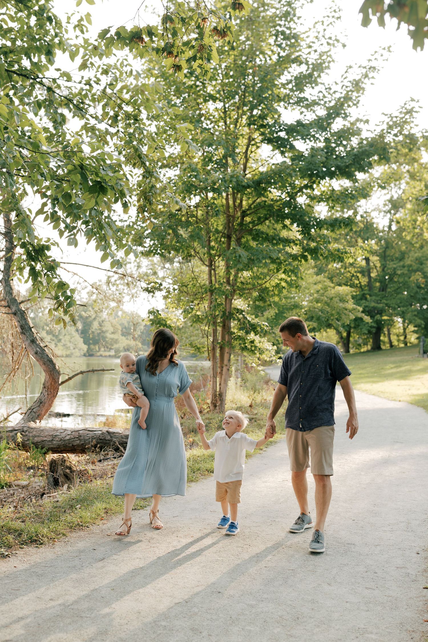 Family walking together on a tree-lined path in a park during golden hour.
