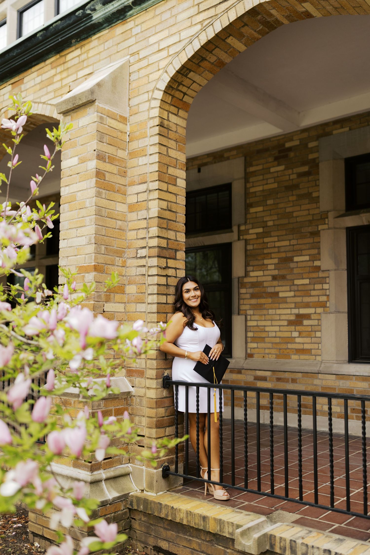 A spring portrait with blooming flowers framing a brick archway and railing.