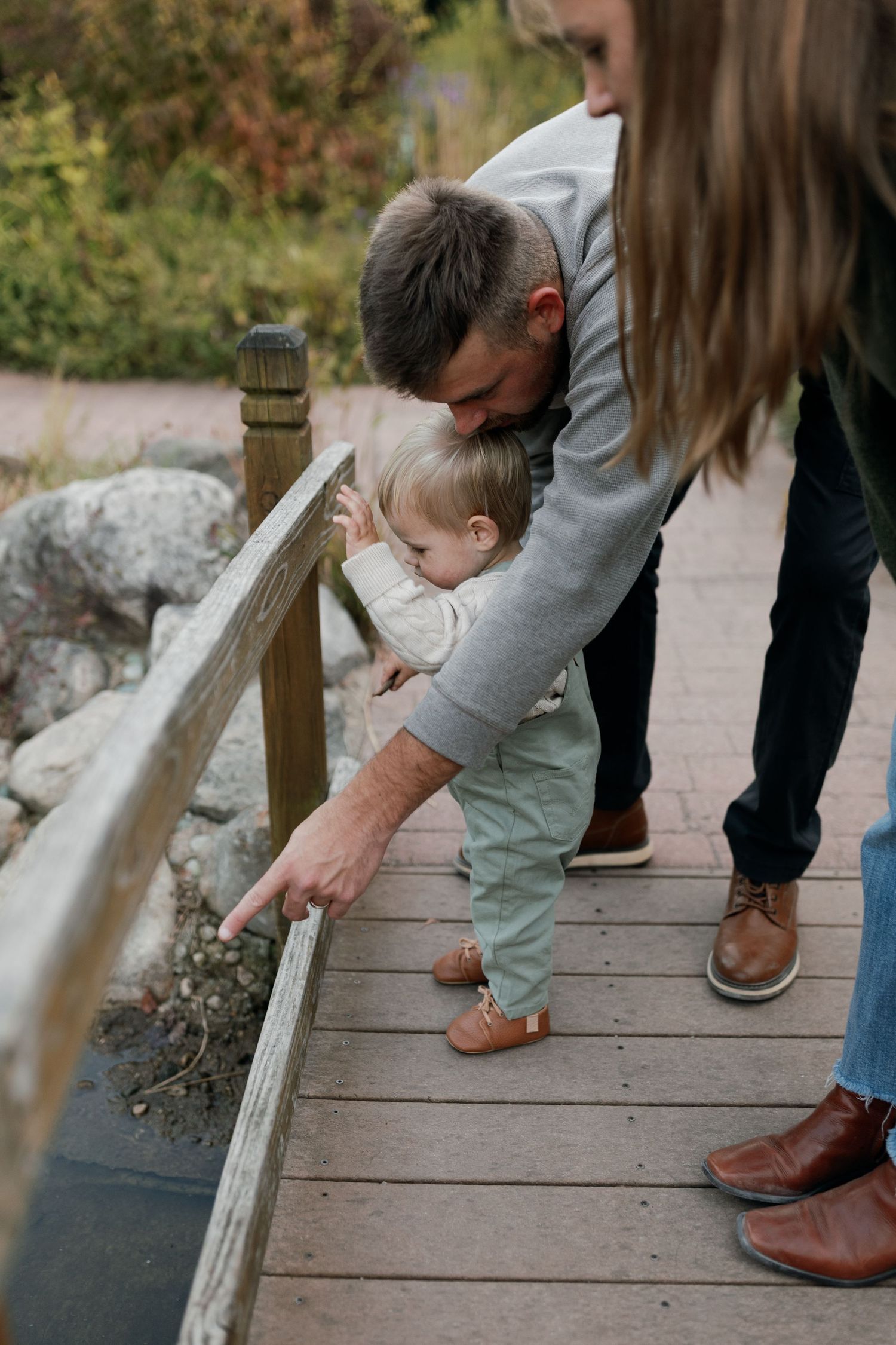 A family exploring together on a wooden deck while pointing at something below.
