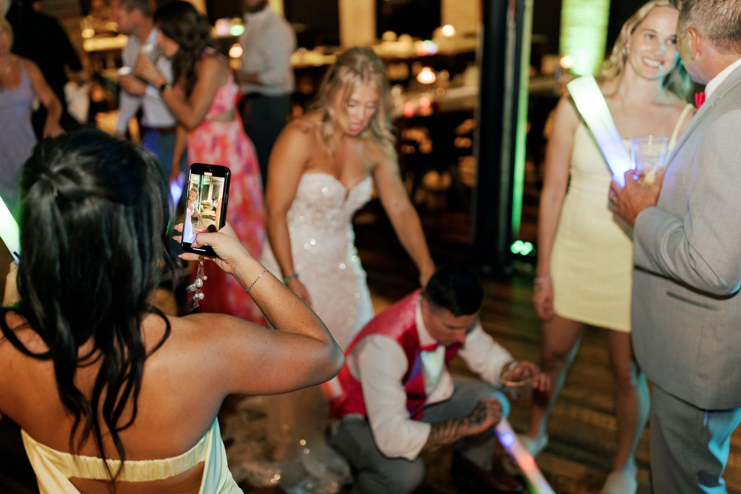Party guests dancing and taking photos on a dance floor during a celebration.