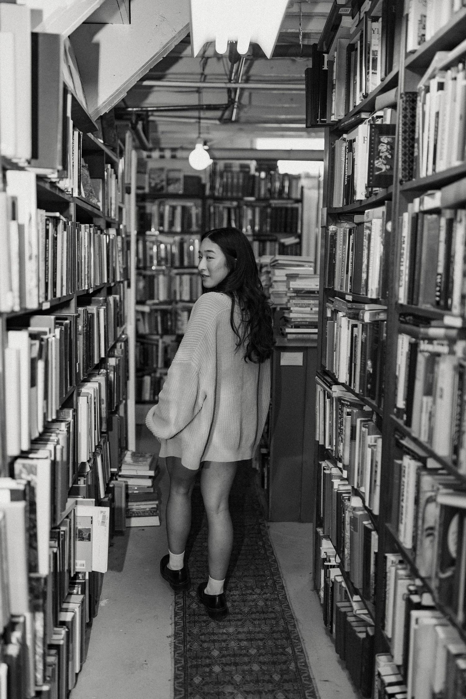 Library stacks with rows of books and narrow aisles in a moody black and white composition.