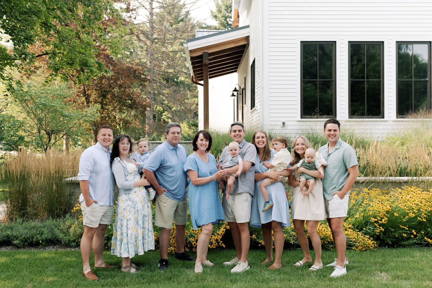 Extended family gathering poses together in coordinated outfits outside a white farmhouse.
