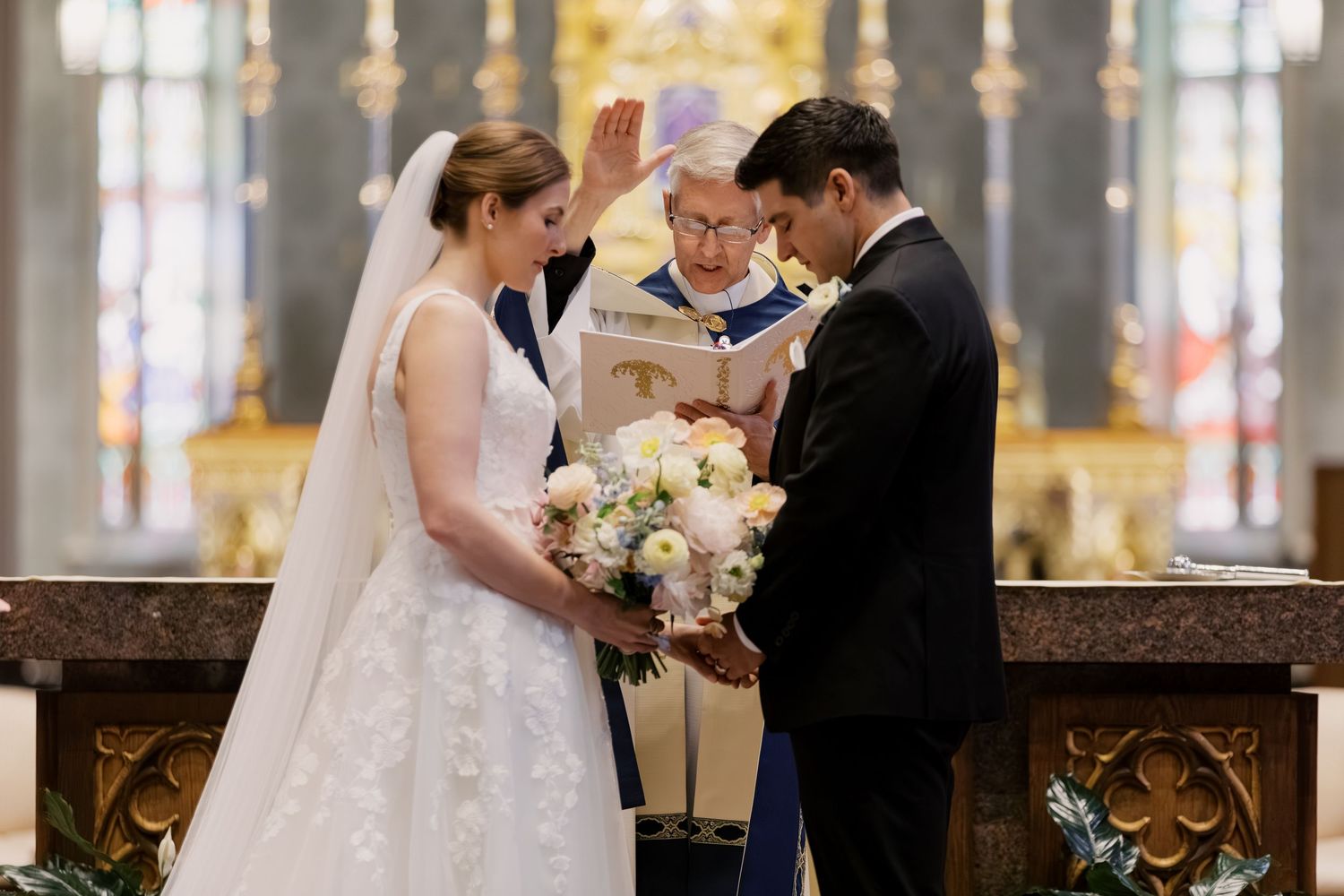 Bride and groom exchange vows at church altar with officiant blessing them during elegant wedding ceremony.