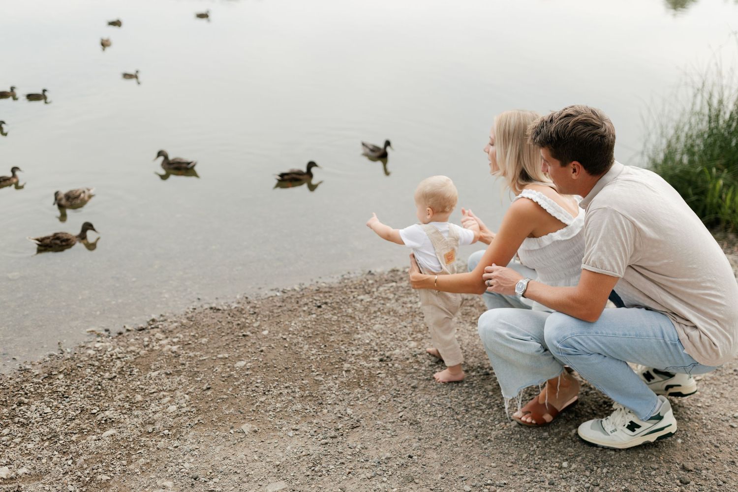 People crouching by lake edge feeding ducks in natural setting.