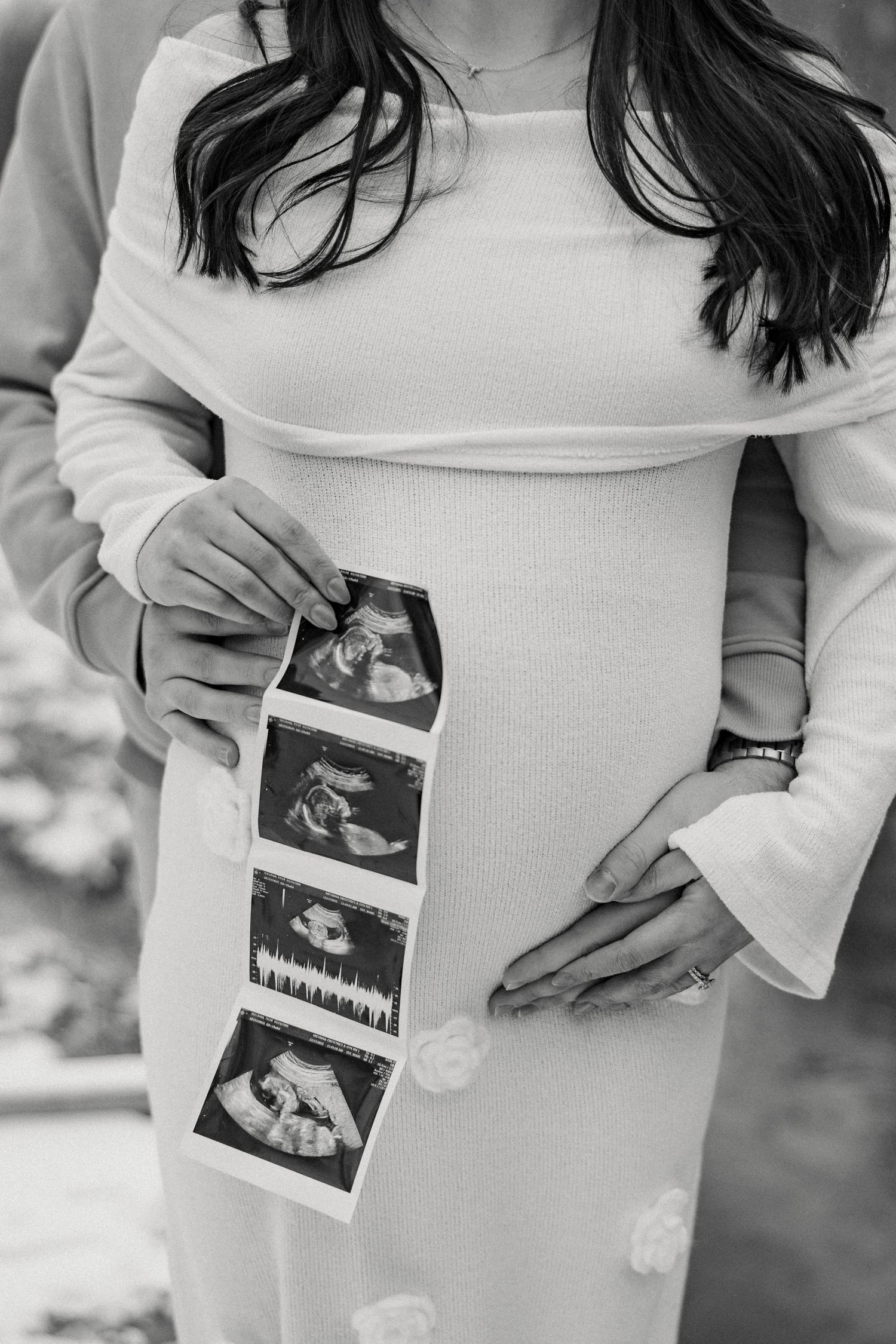 Person in white dress holding ultrasound photos during pregnancy announcement photoshoot.