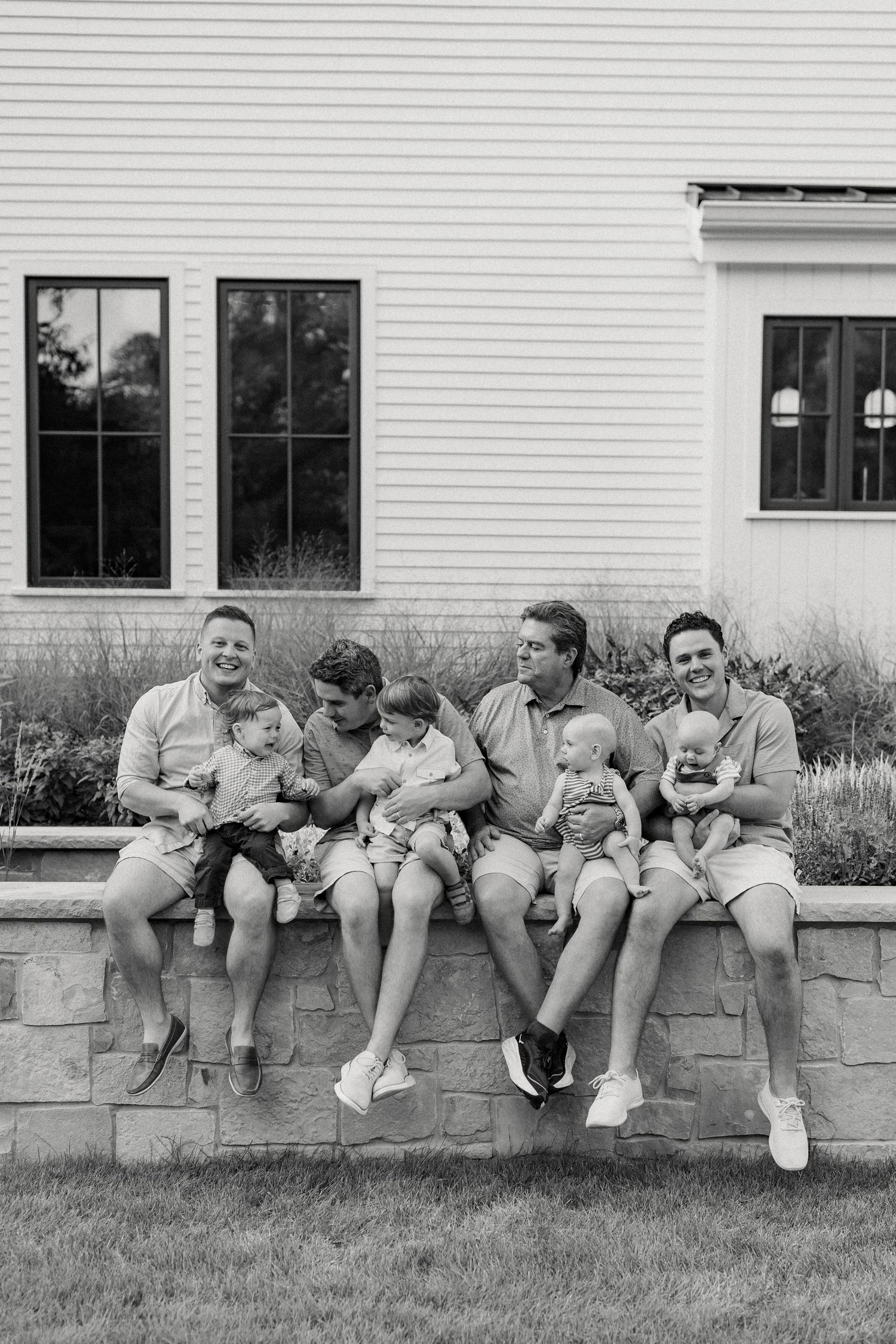 Group lounging casually on stone wall outside white building in coordinated neutral outfits.