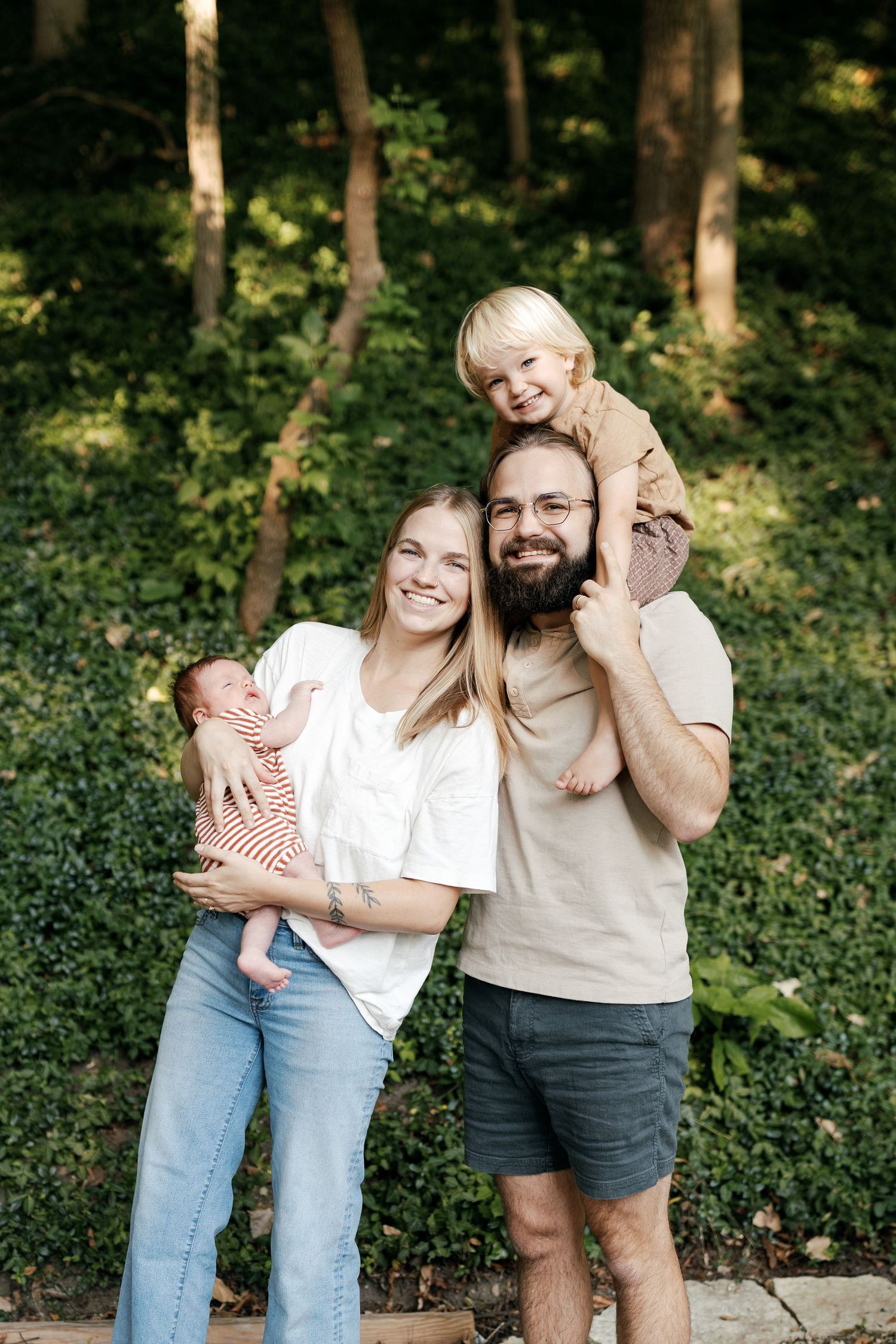 A joyful family photo session in a wooded setting with natural sunlight filtering through the trees.