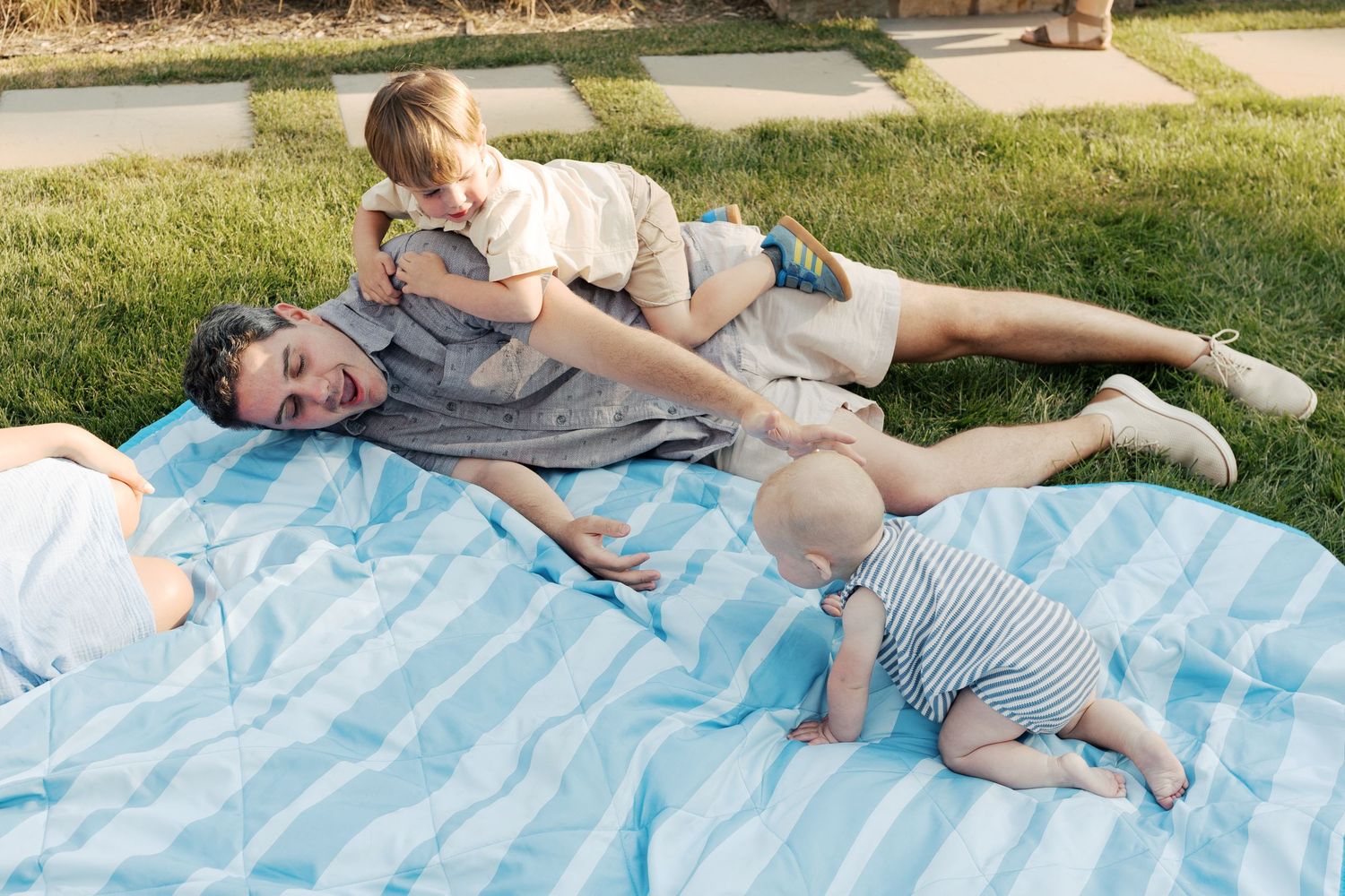Family relaxing on blue picnic blanket in sunny backyard setting.