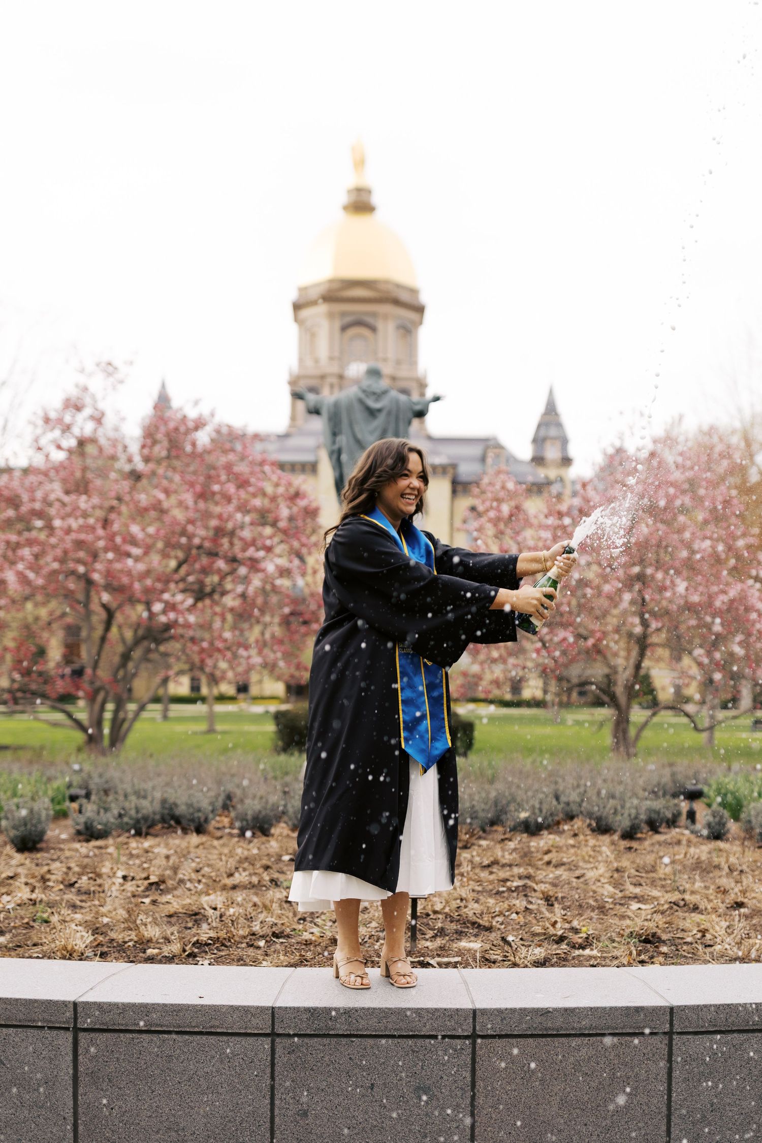 Someone in a black jacket enjoys spring cherry blossoms while taking photos in a scenic park setting.
