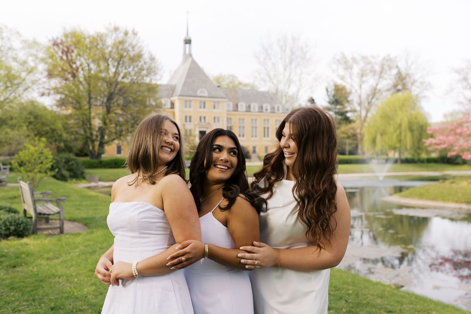 Friends celebrate graduation together on campus with golden university building in background.