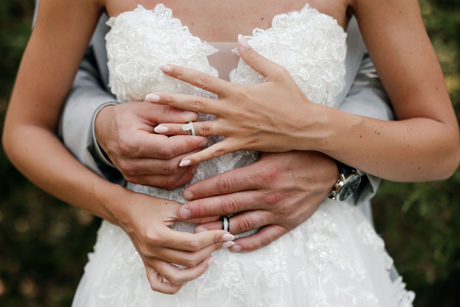 Close-up shots of hands wearing wedding rings against a white lace dress background.