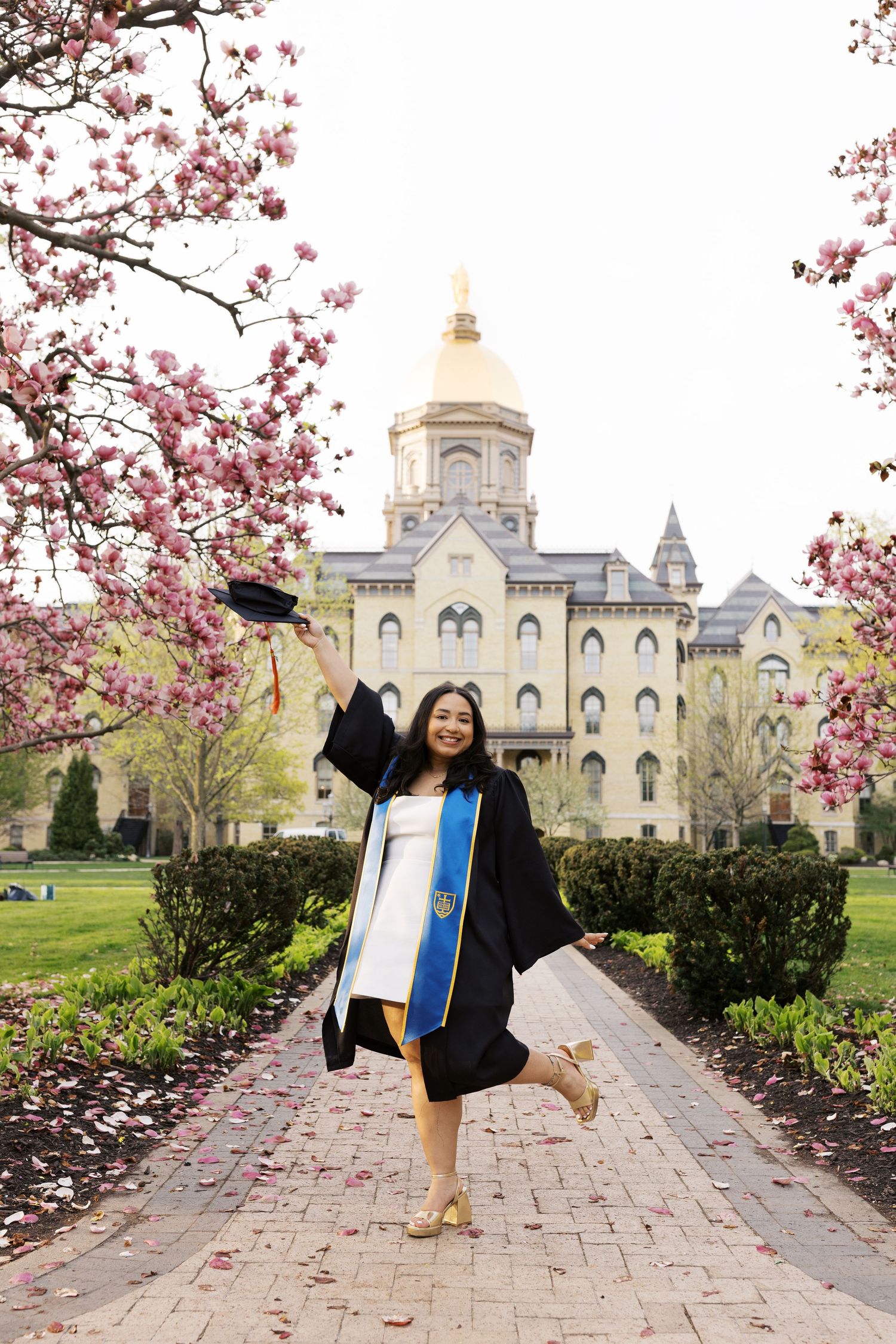 Graduate celebrating in cap and gown with cherry blossoms framing Notre Dame's Golden Dome.