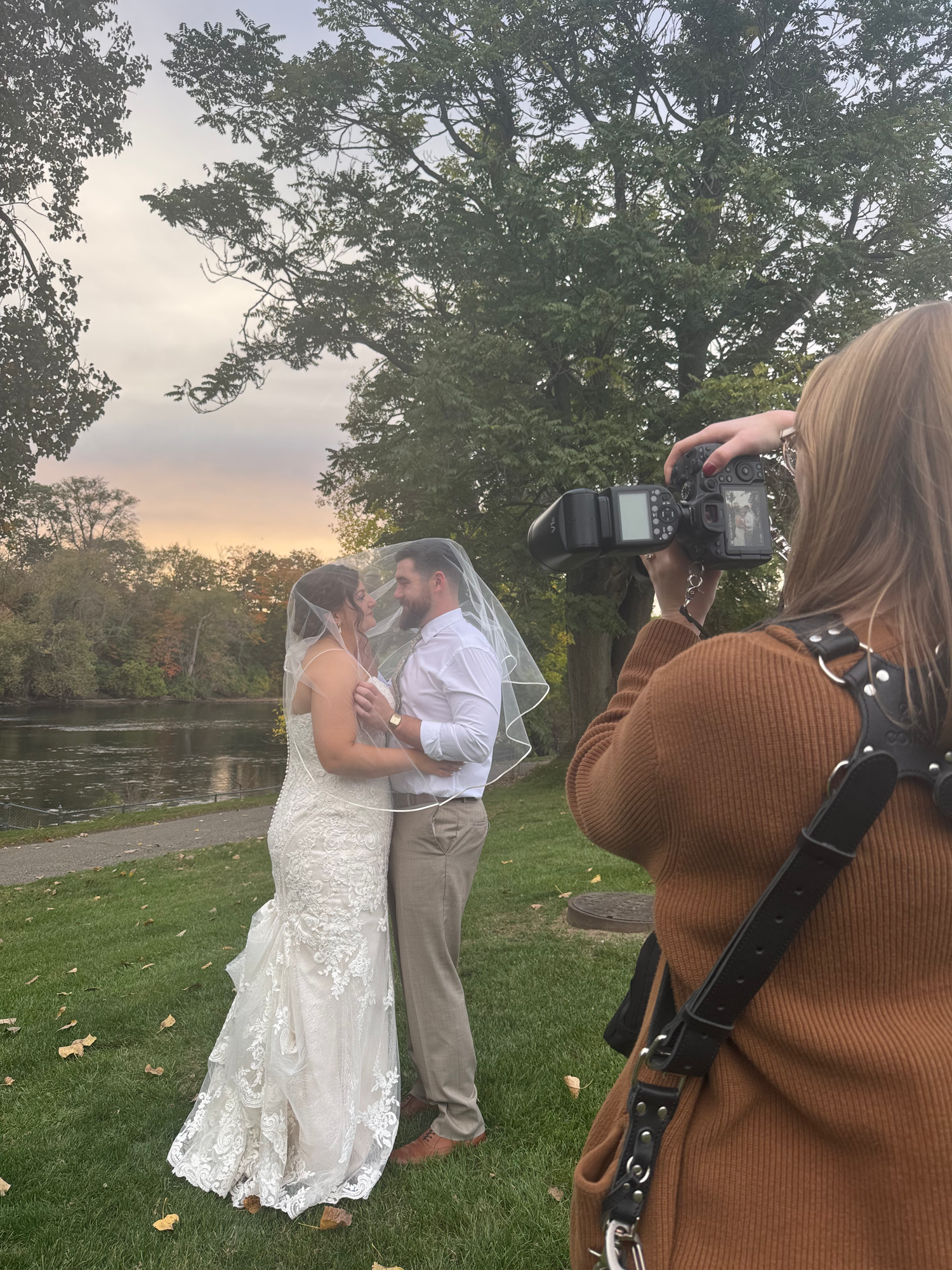 Behind the scenes of a wedding photoshoot in a natural outdoor setting at sunset.