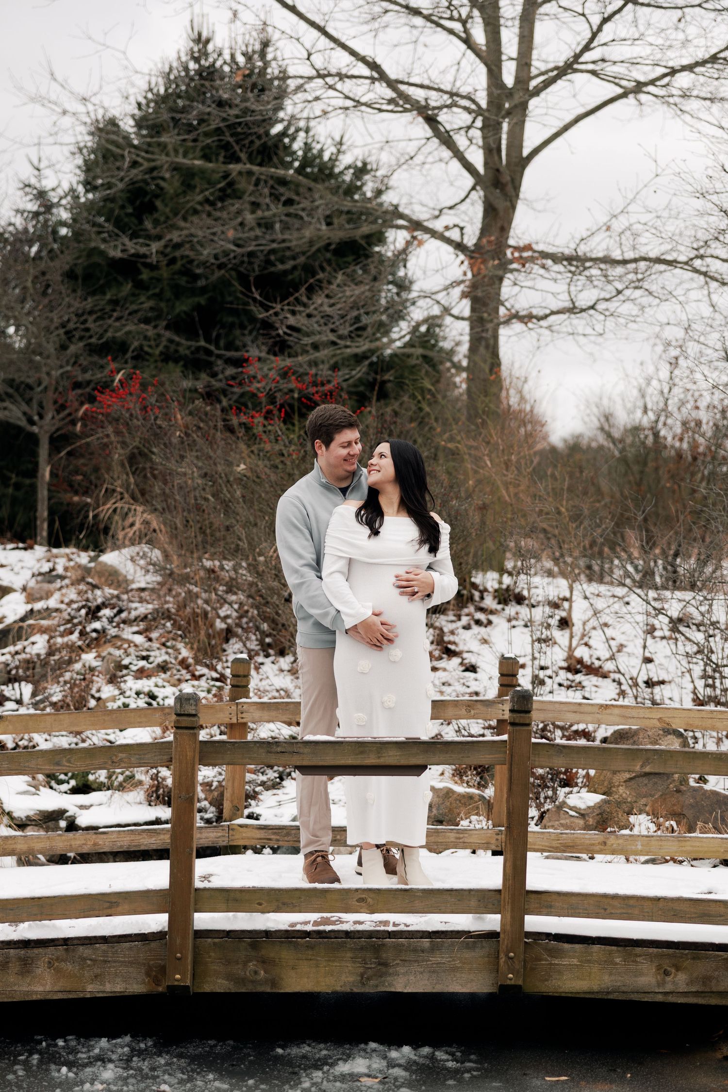 Couple standing on a snowy wooden bridge during winter engagement photoshoot.