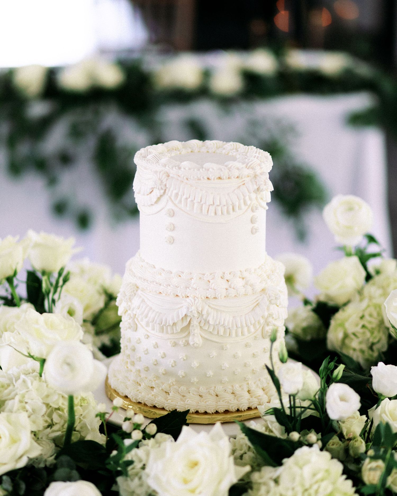 Elegant white wedding cake with lace piping details surrounded by fresh white roses.
