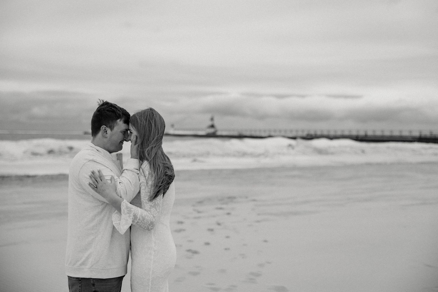 Black and white romantic beach engagement photos showing intimate moments between a couple on a sandy shore.