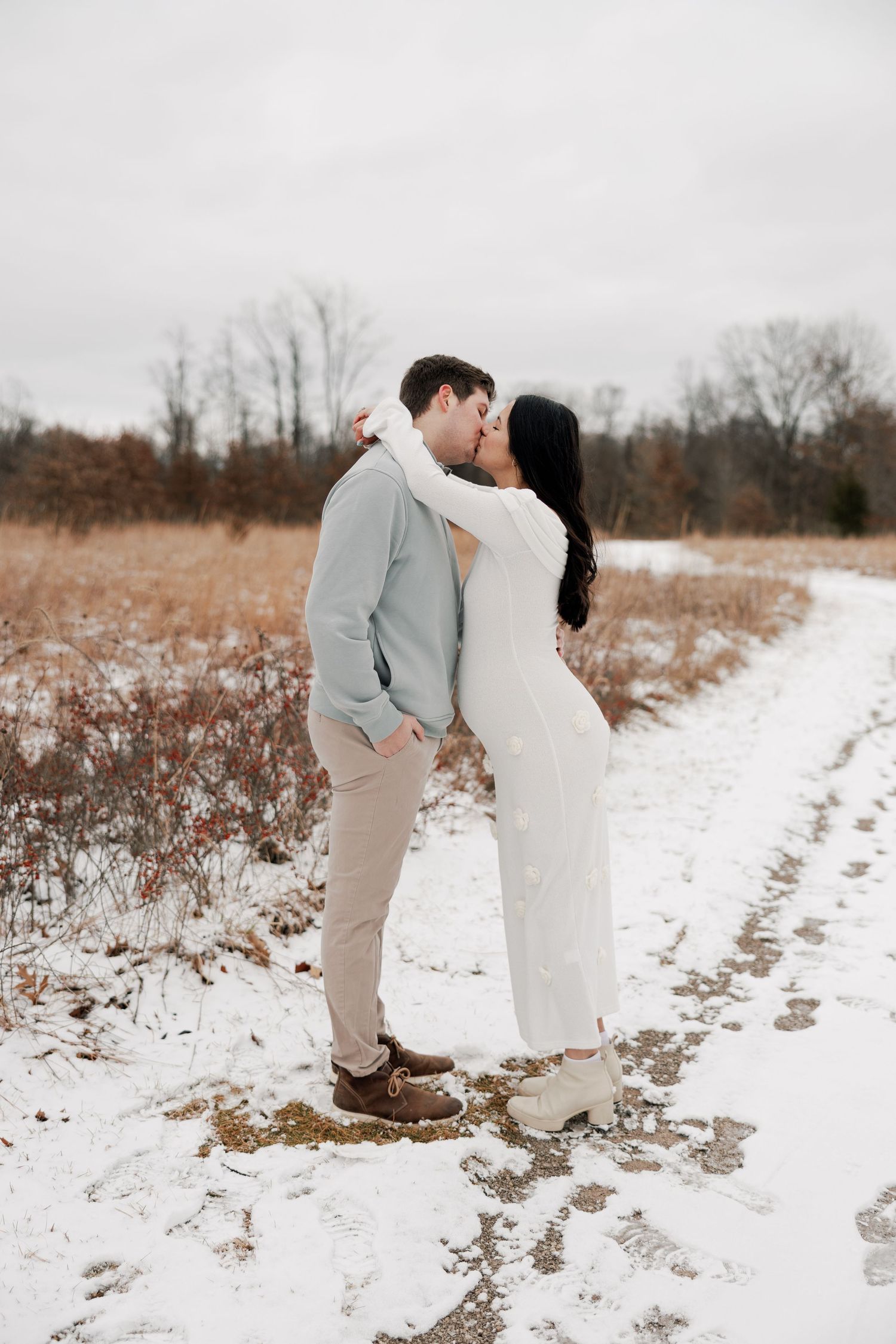 An intimate moment between a couple sharing a kiss in a winter landscape with snow on the ground.