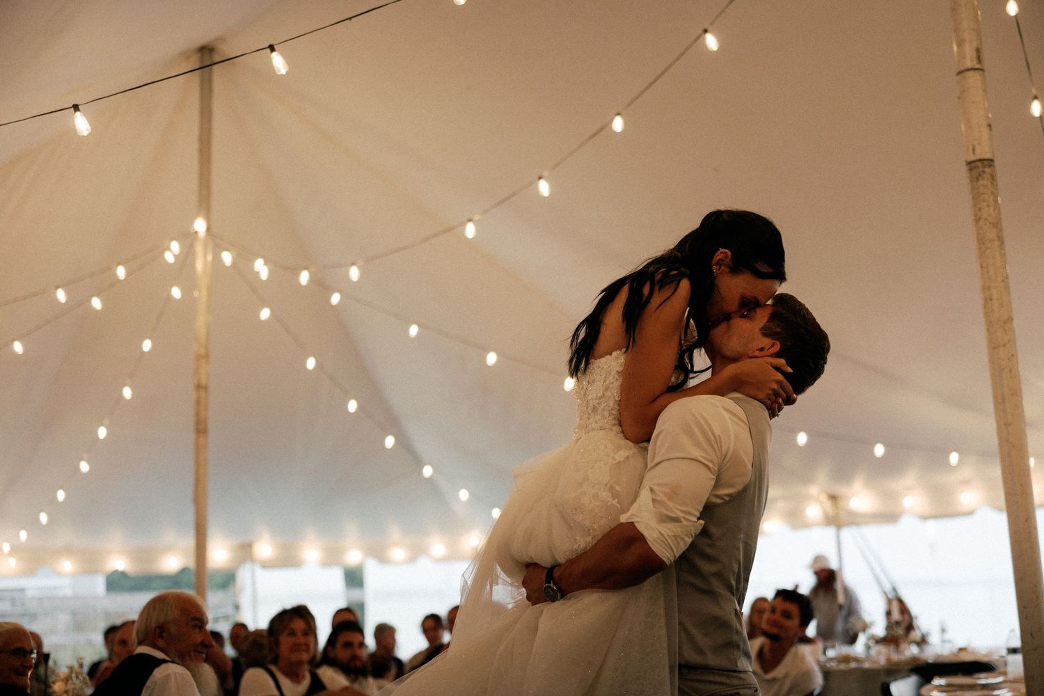 Couple sharing a romantic dance under twinkling lights in a wedding tent reception.