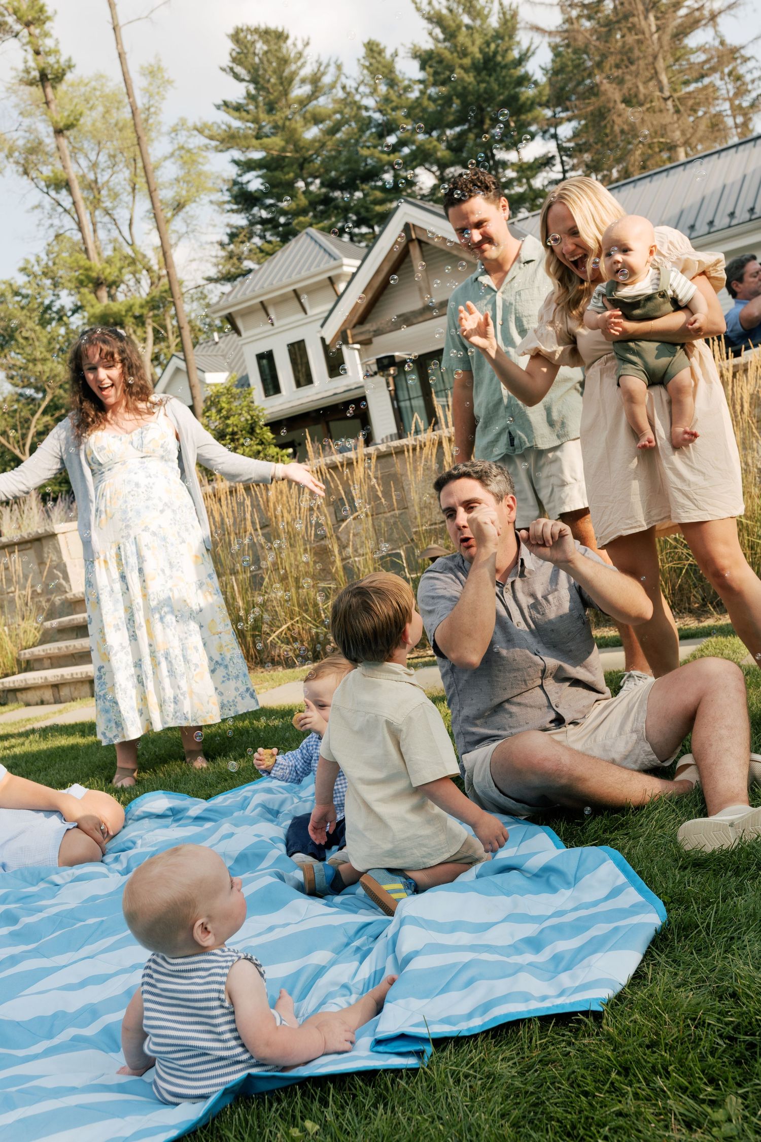 Family plays together on a blue blanket in their backyard on a sunny day.