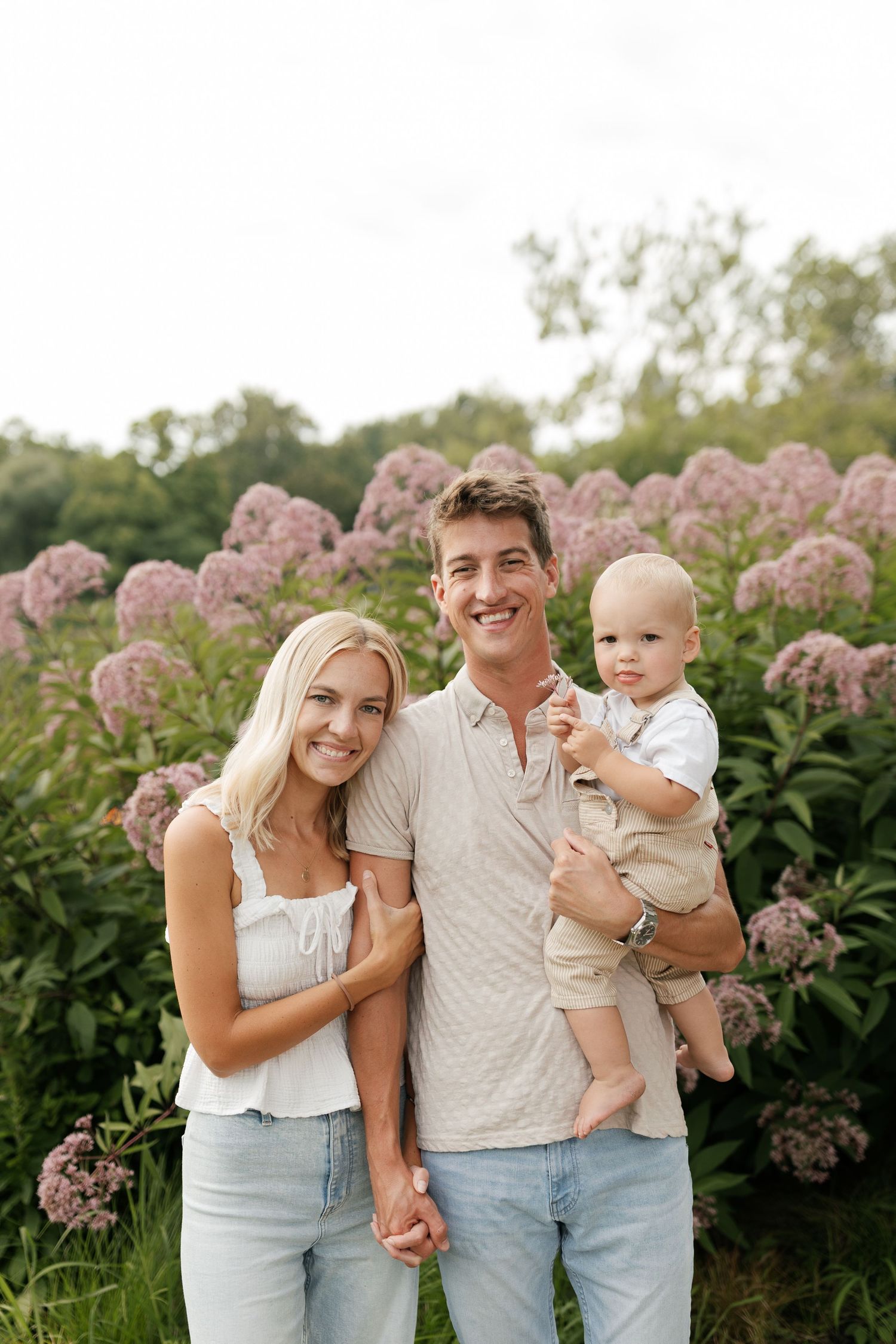 Family posing together in front of blooming pink hydrangea flowers on a summer day.
