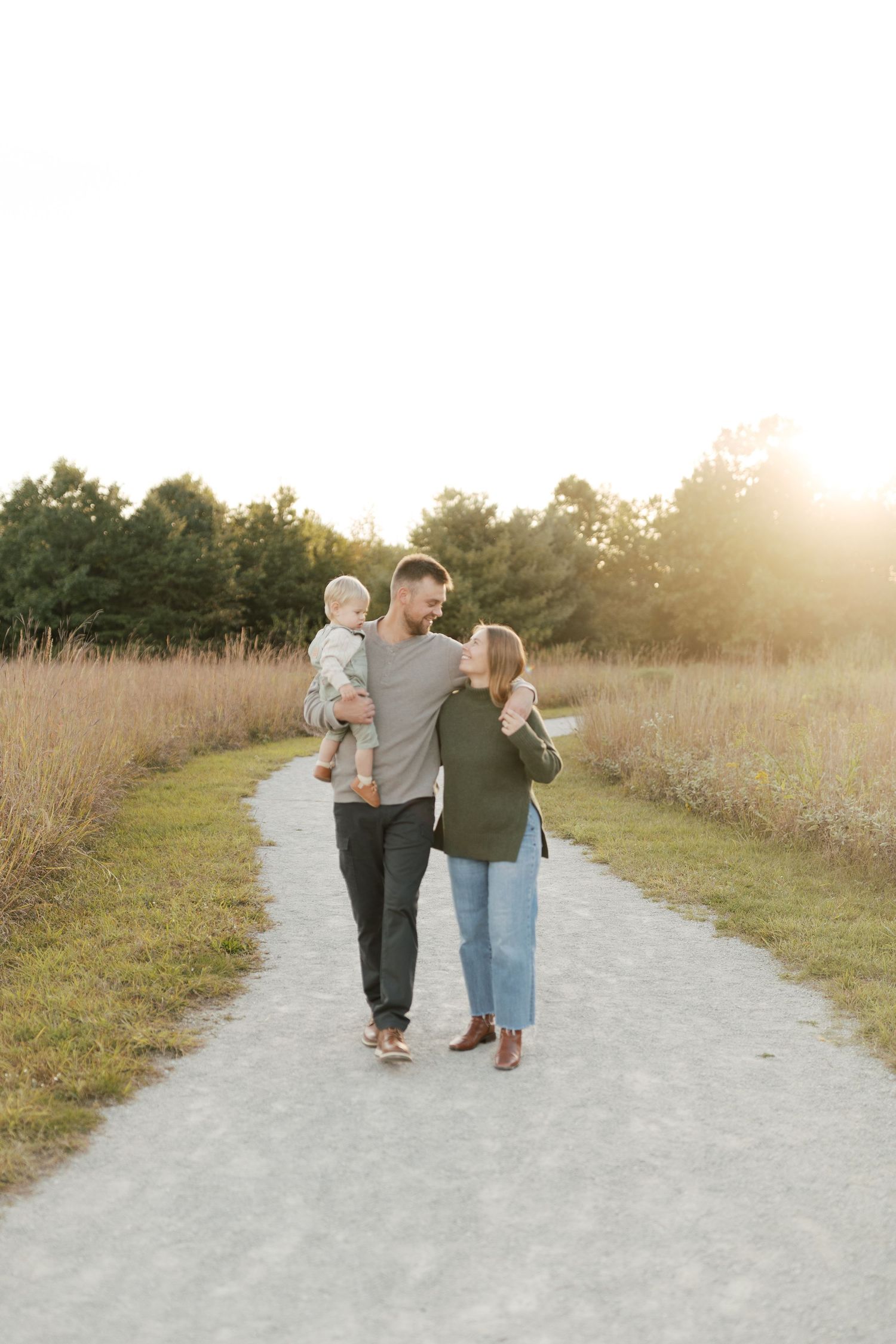 A family strolling together on a path through tall grass during sunset.