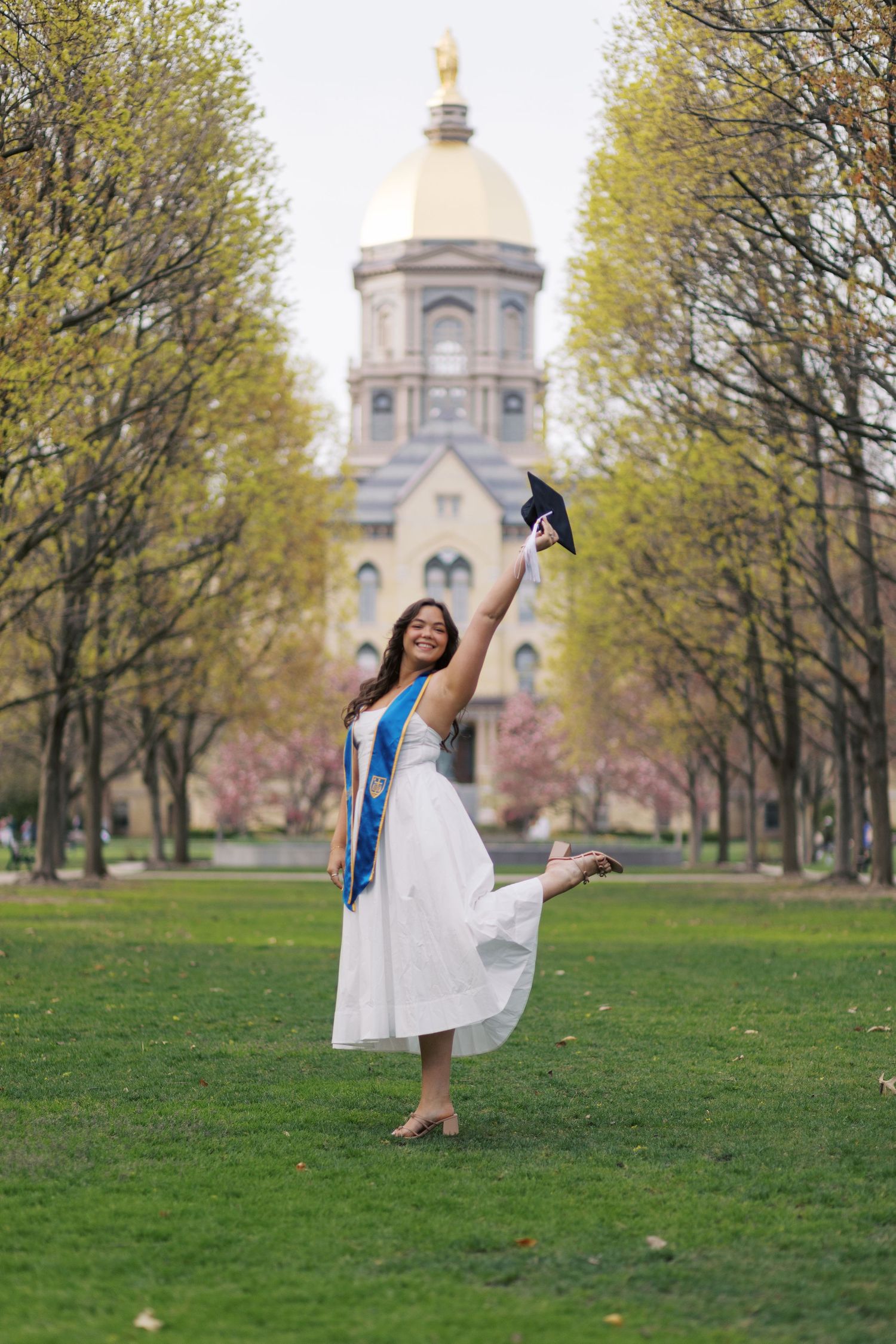 A composite photo showing a person in a flowy white dress dancing joyfully on a green lawn with a domed building in background.