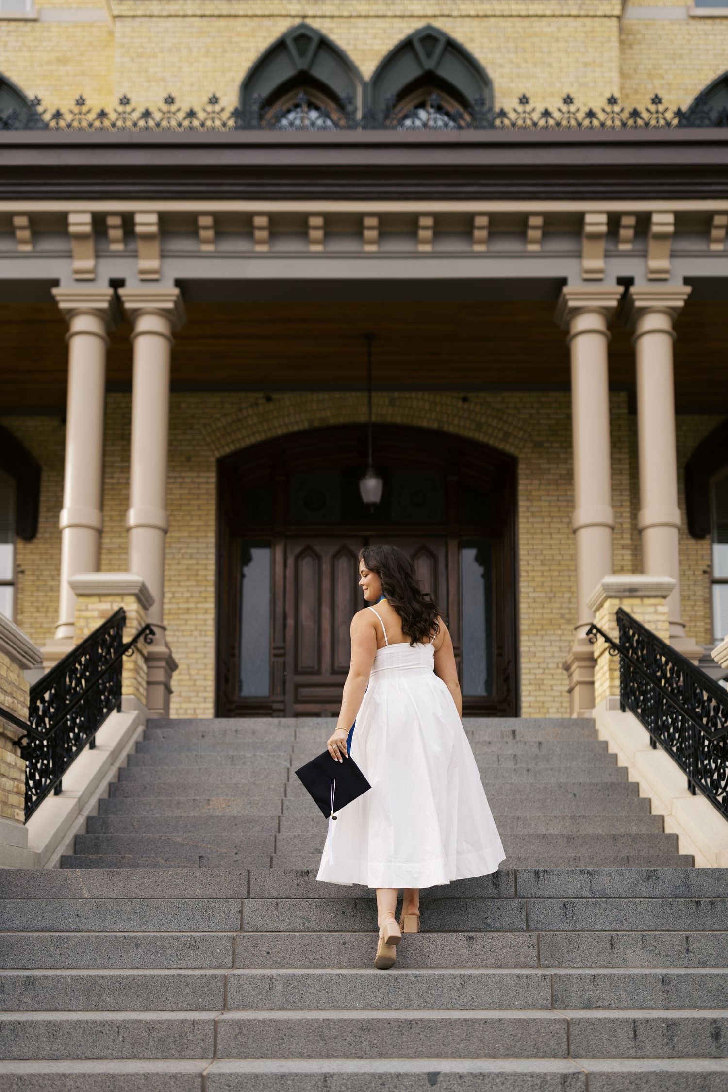 Person in white dress ascends stone steps of historic building with yellow brick facade and Gothic architectural details.