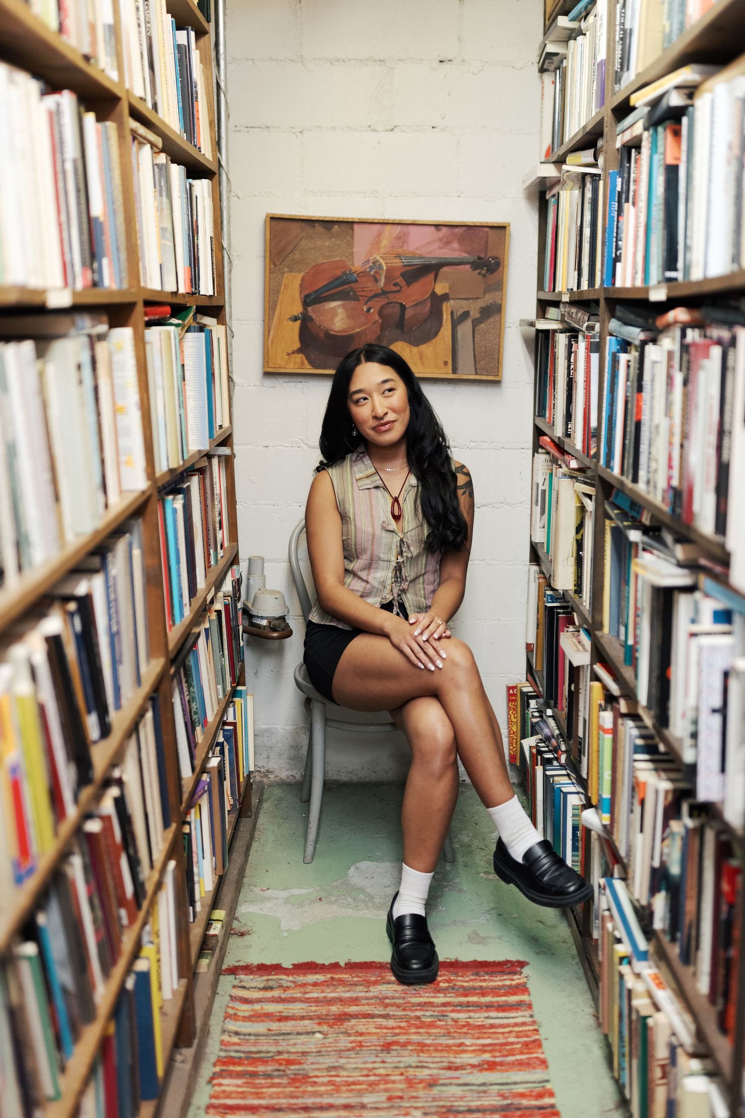 Person sitting between library bookshelves on a patterned rug for a photo shoot.