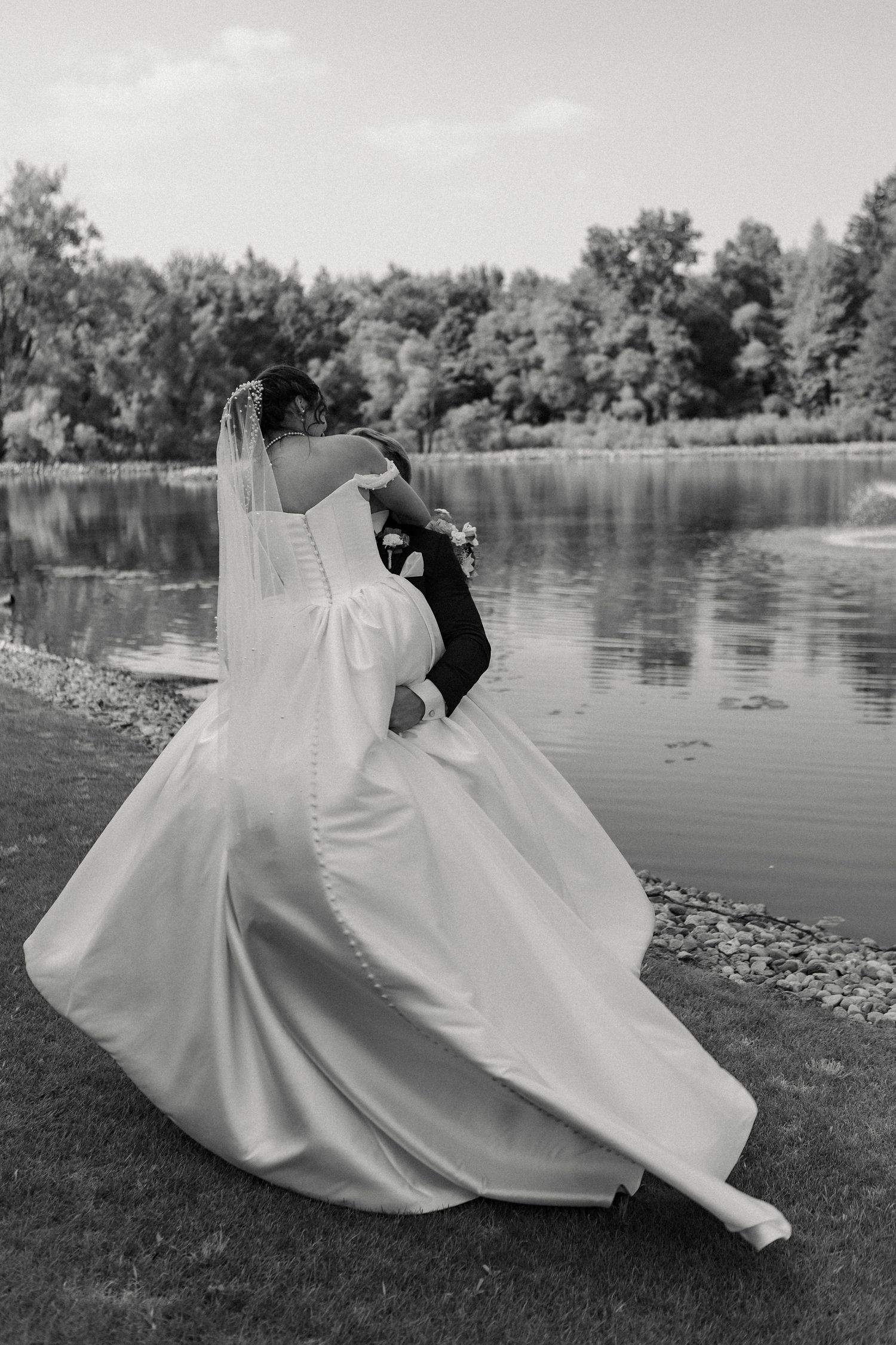 A dramatic black and white photo of a flowing wedding dress by a serene lake.