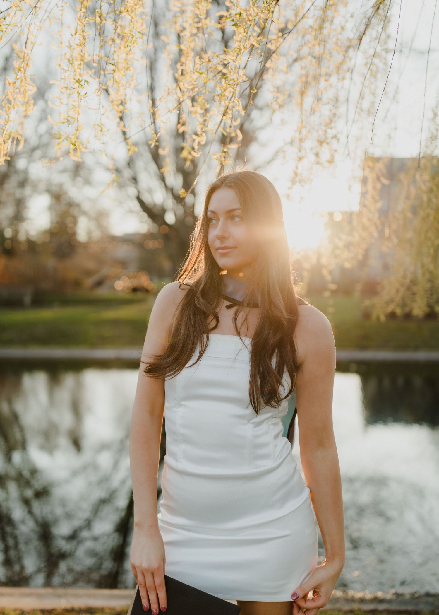 White dress silhouette against golden sunset by lake with overhanging branches.