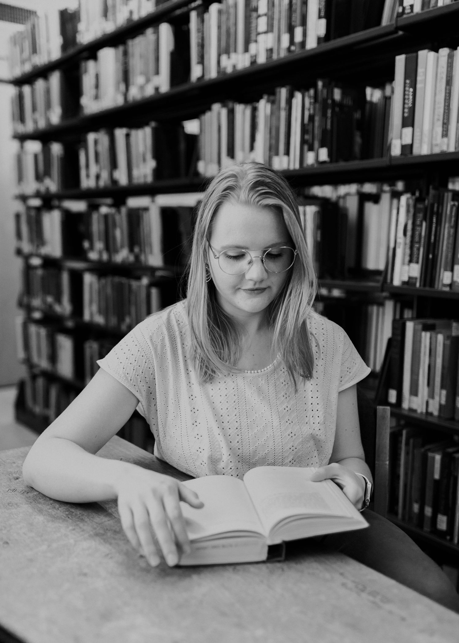 Student studying from a book in library with bookshelves in background.