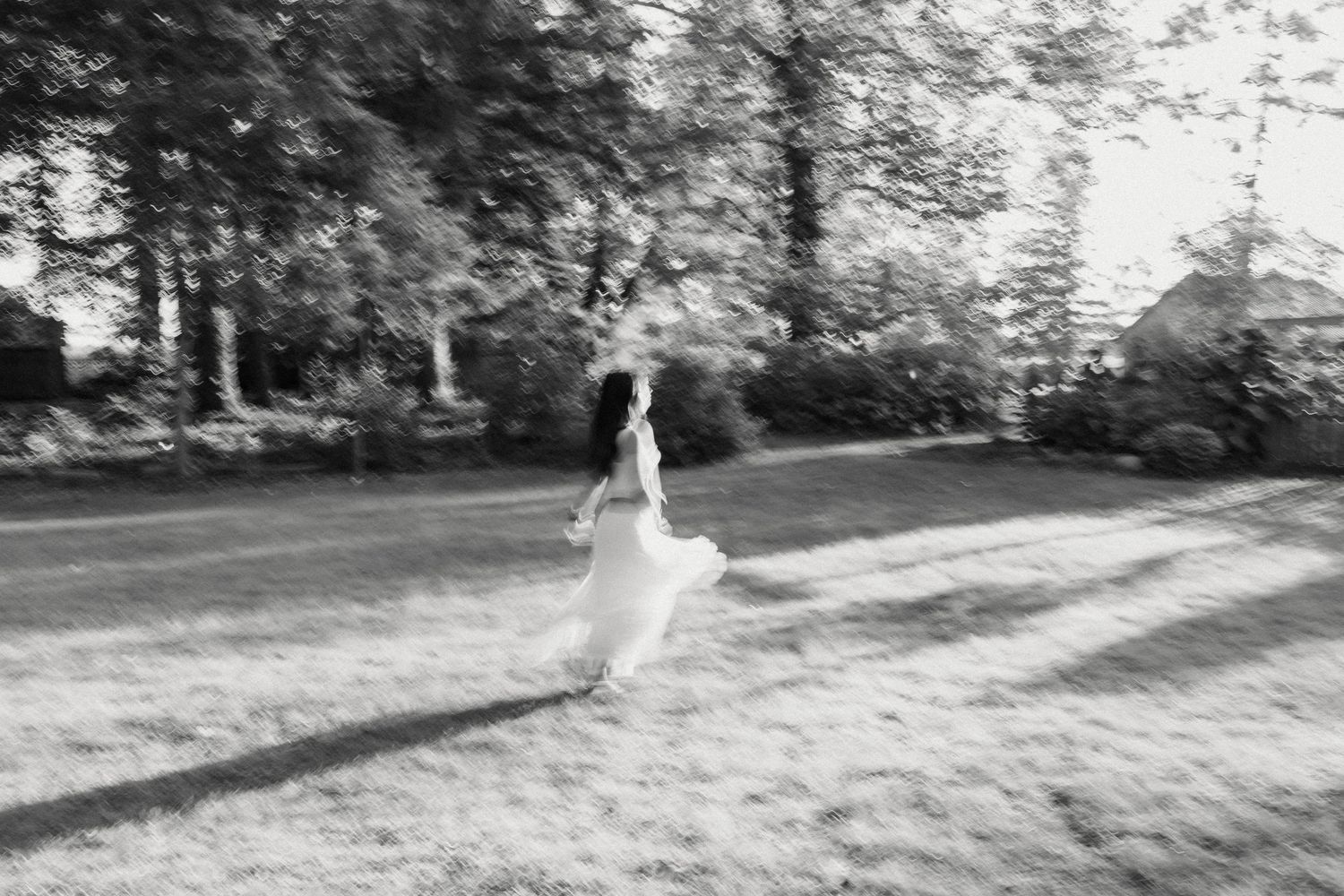 Blurred motion shot of a bride in a white dress running across a sunlit lawn.
