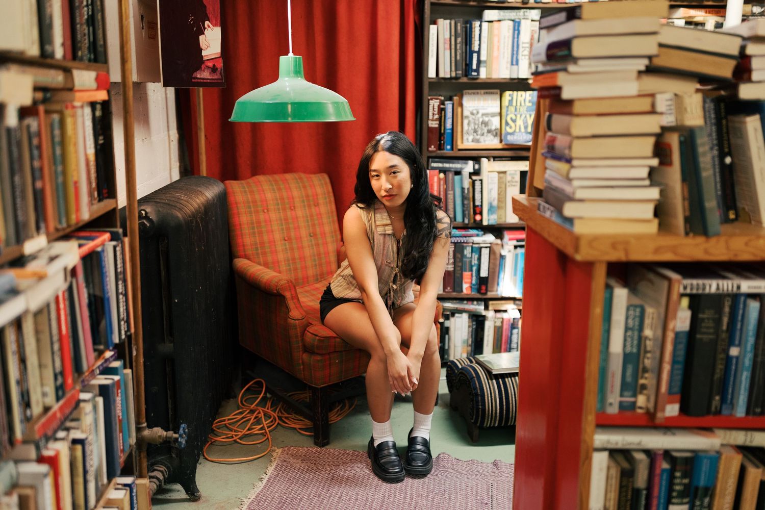 Artistic photoshoot among library bookshelves with red curtain backdrop.
