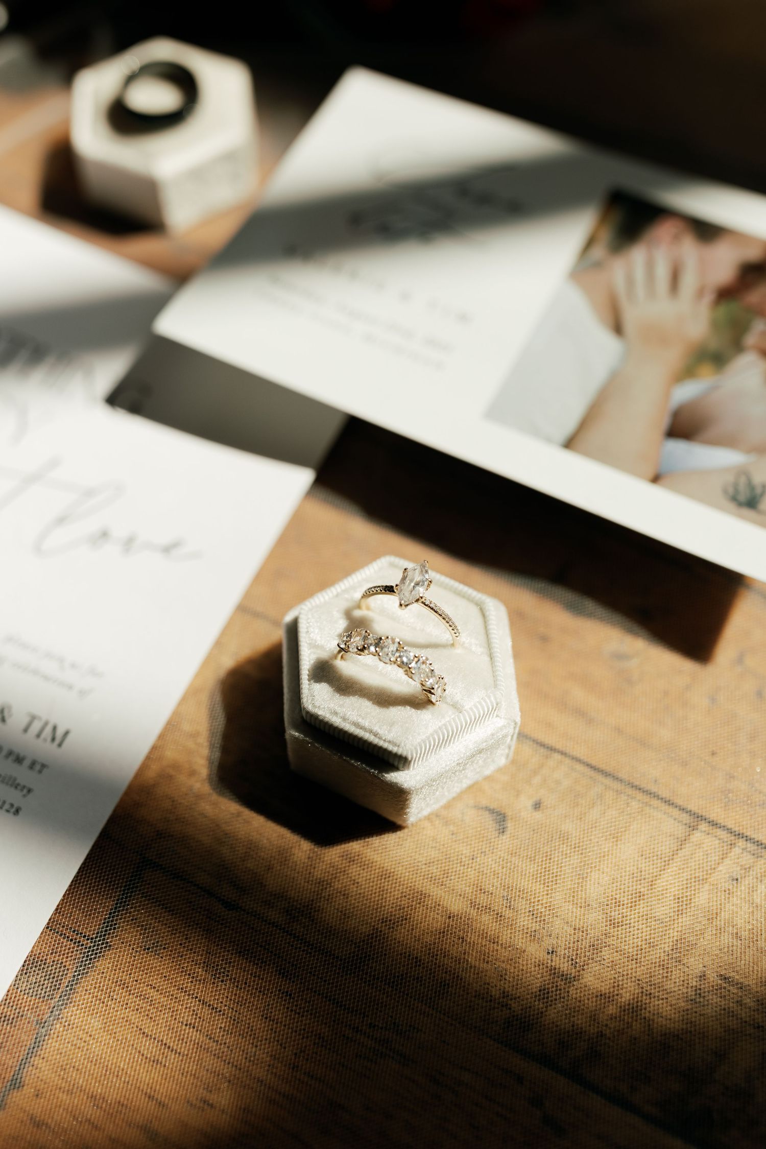 Wedding details featuring an engagement ring in a hexagonal box alongside invitation cards on a wooden surface.