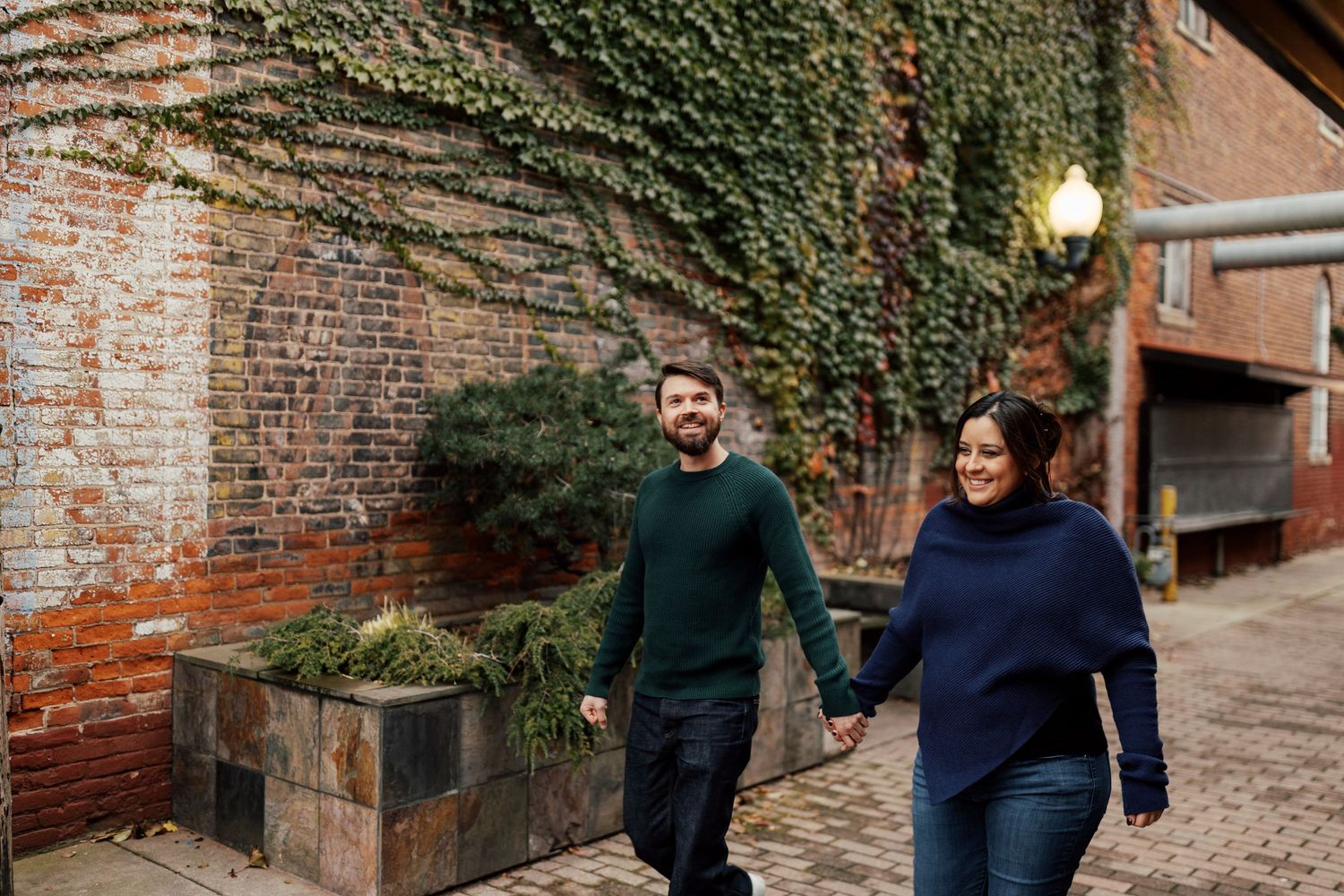 Couple walking along ivy-covered brick wall exterior.
