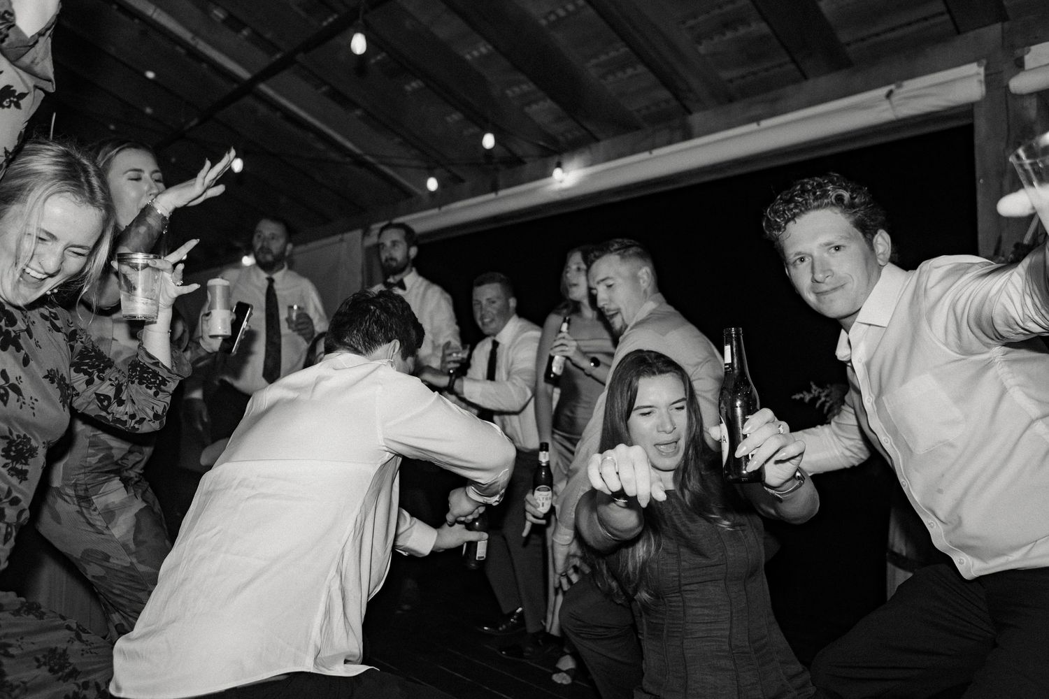 Wedding guests dance and celebrate on a rustic wooden dance floor under string lights.