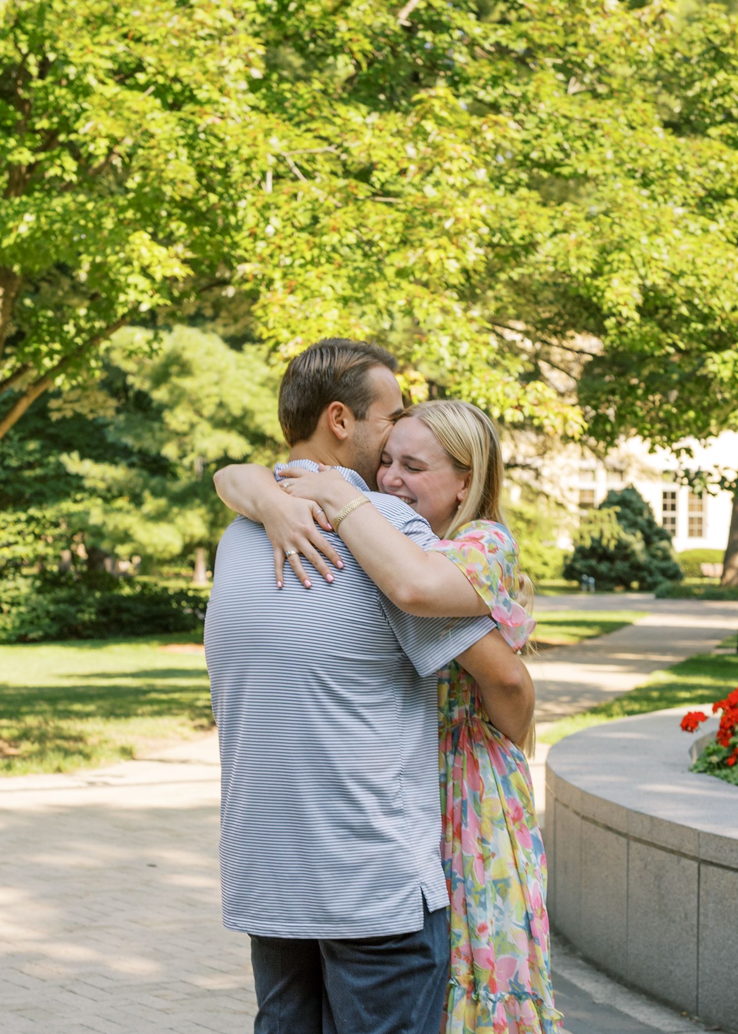Two people sharing an emotional embrace in a garden setting with green trees.