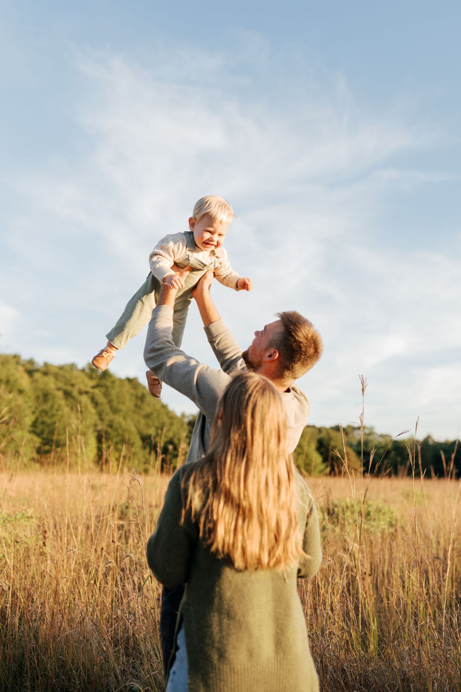 A joyful family moment in a golden field with a child being lifted into the air.