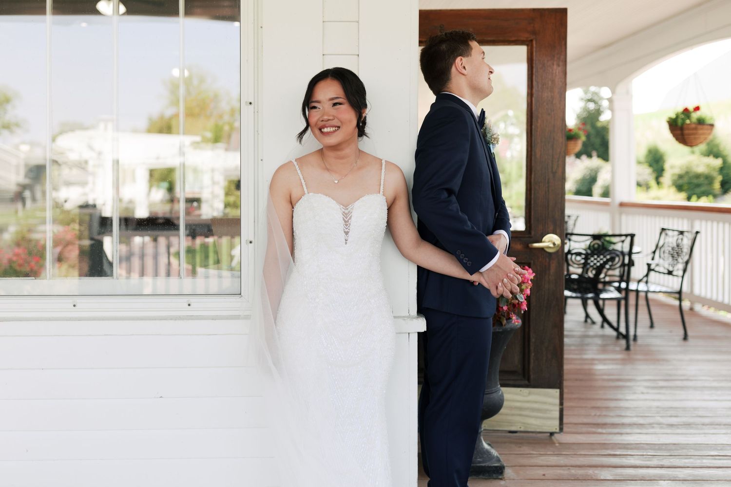 First look wedding photo with couple separated by white wall on porch.