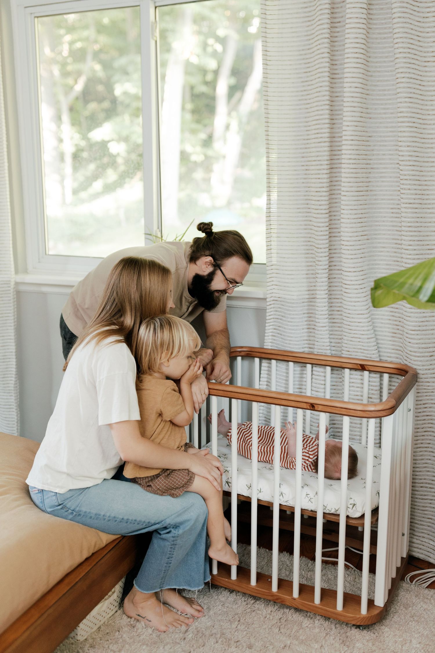 Emotional family moments captured near a wooden crib by window light.