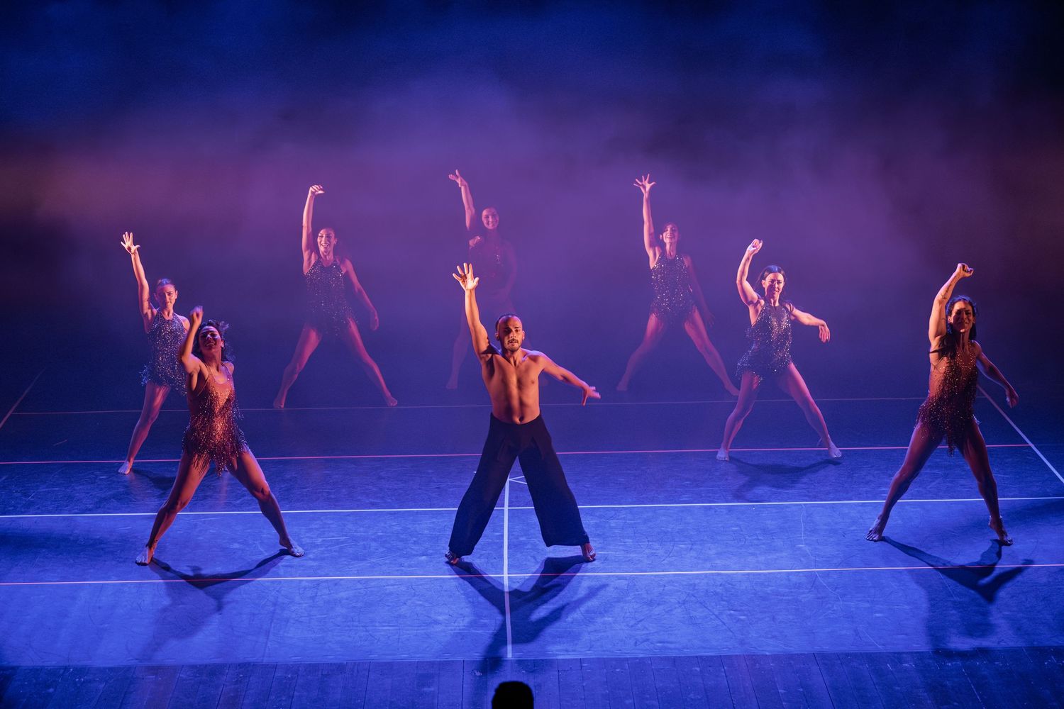 Modern dancers perform on stage in blue lighting with dynamic movements and graceful poses during a contemporary dance show.